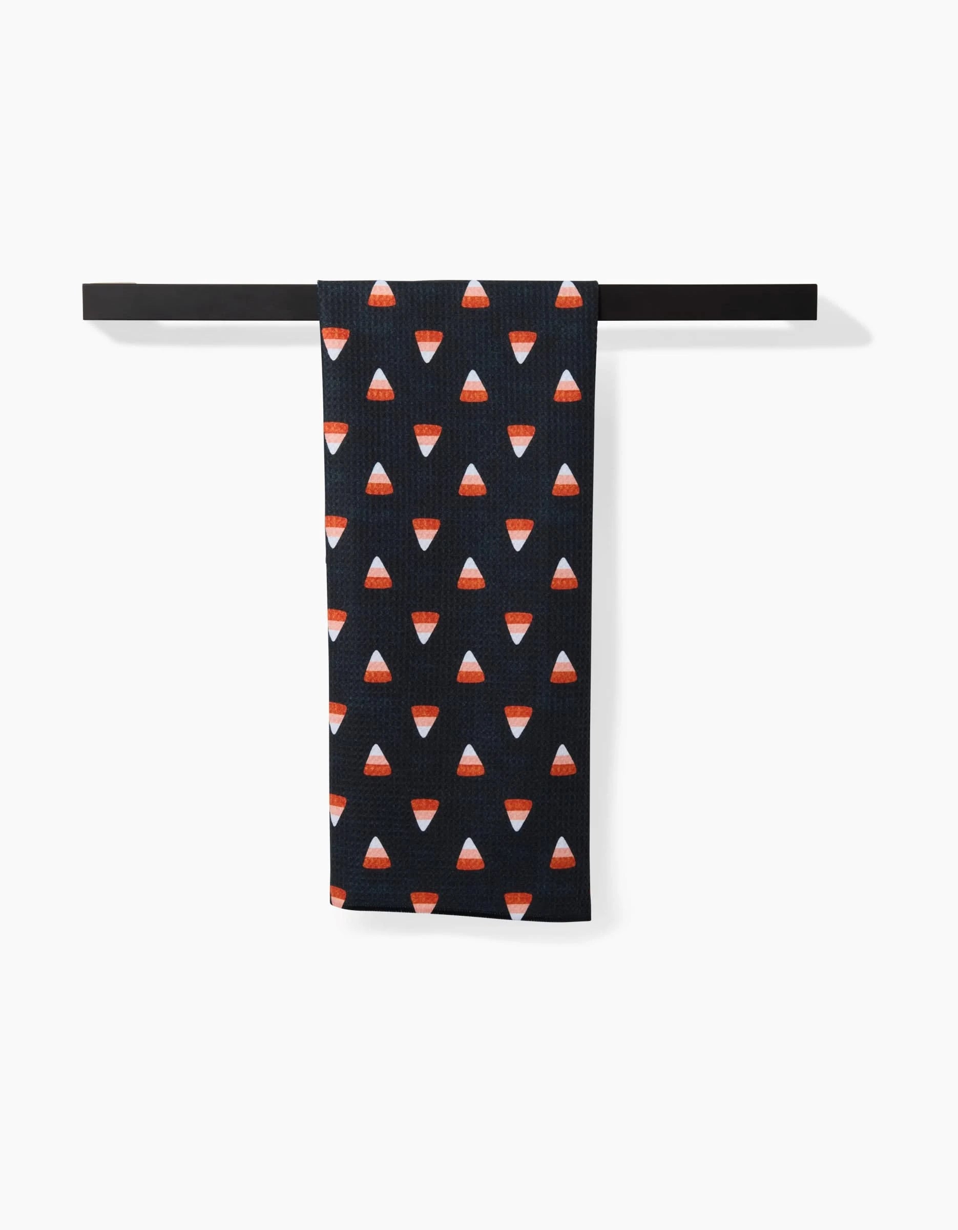 The Linnet black tea towel by Amy MacCready, featuring a repeating candy corn pattern on durable Geoweave fabric, hangs neatly on a black towel bar against a white background.