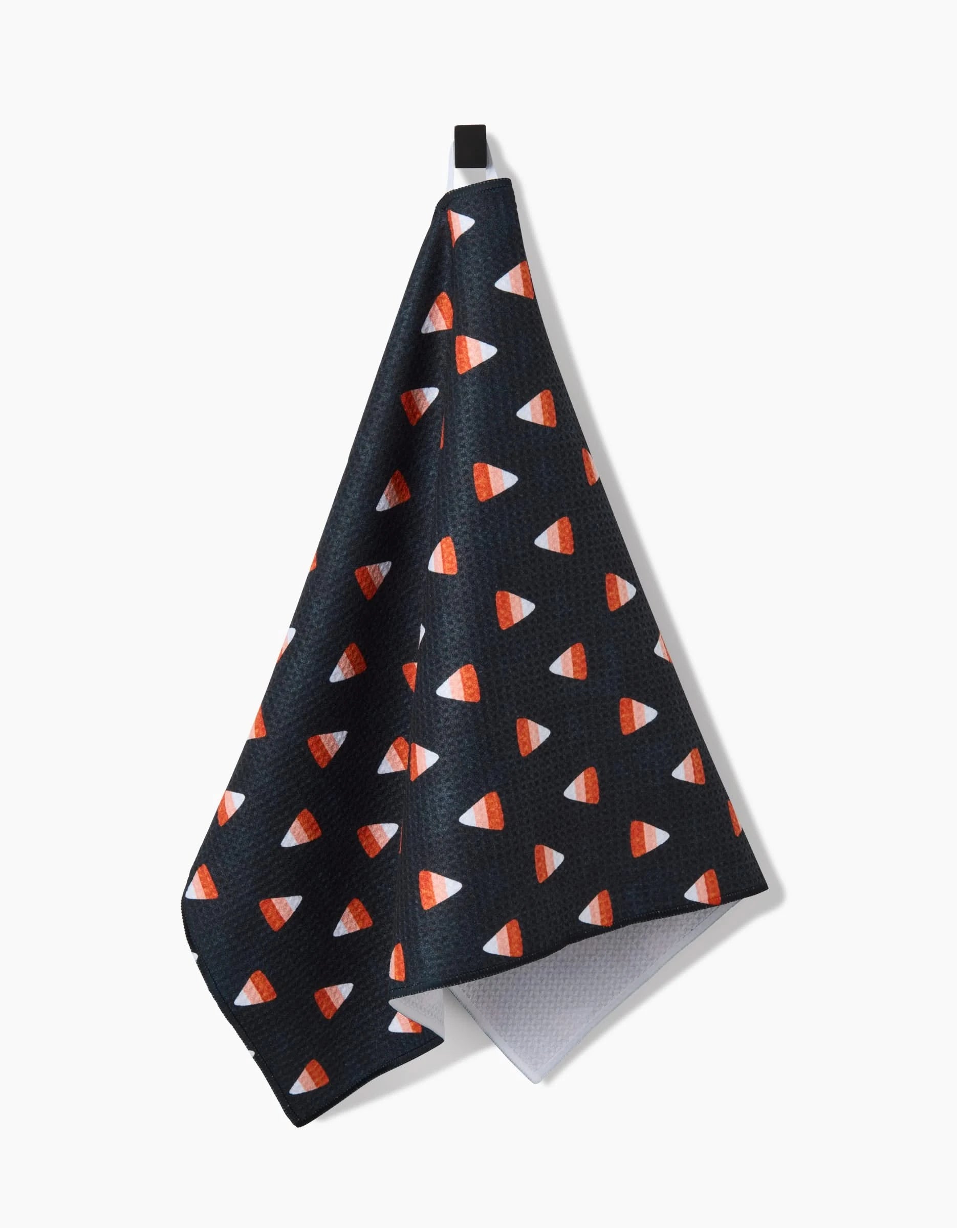 The Linnet by Amy MacCready is a black kitchen tea towel made from recycled materials, featuring a repeating candy corn pattern and hanging from a black loop against a white background.