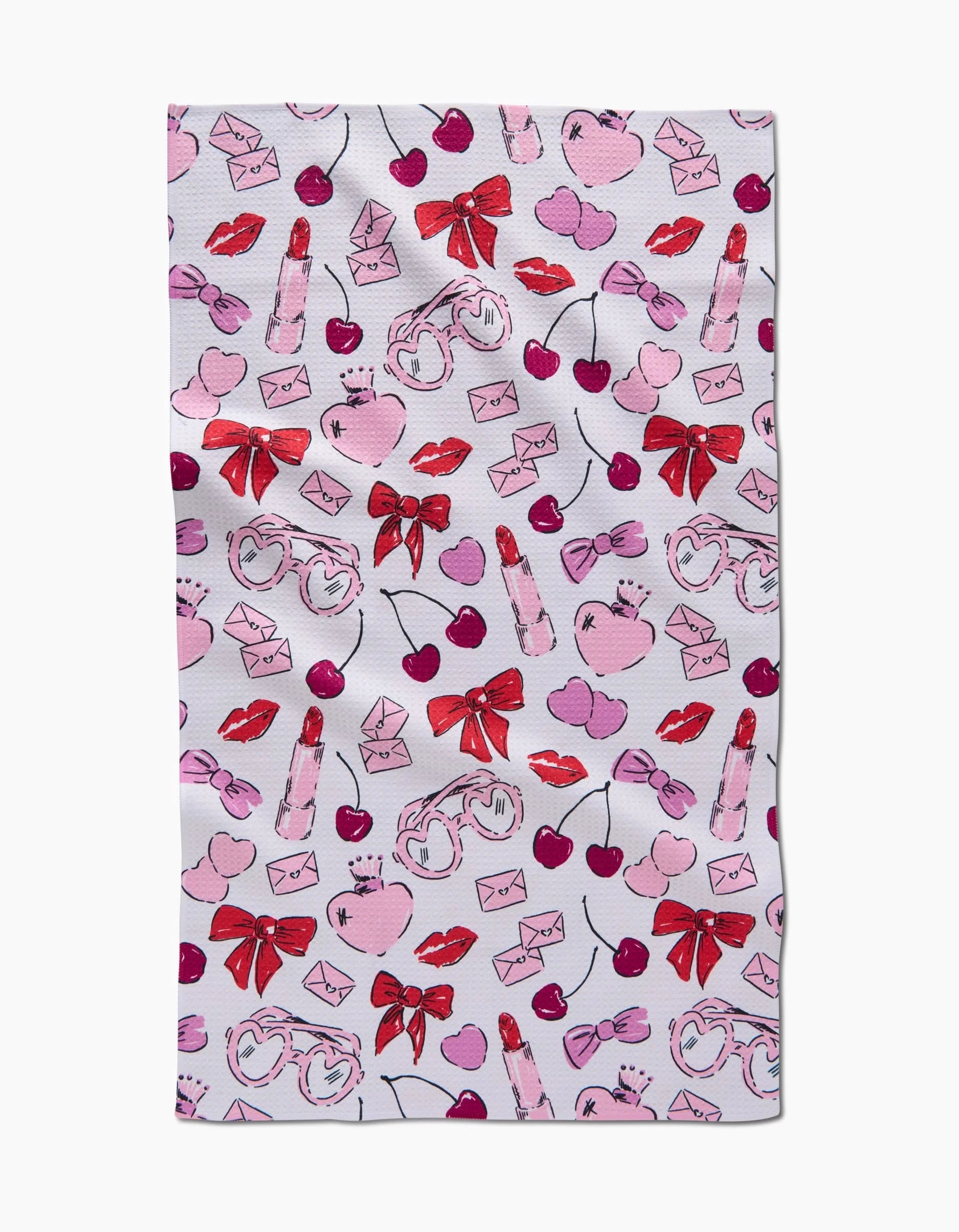 The Lip Smacking Good tea towel by Hufton Studio is a playful and romantic white cloth featuring a charming repeating pattern of pink hearts, red lips, bows, cherries, lipstick tubes, love letters, and heart-shaped glasses.