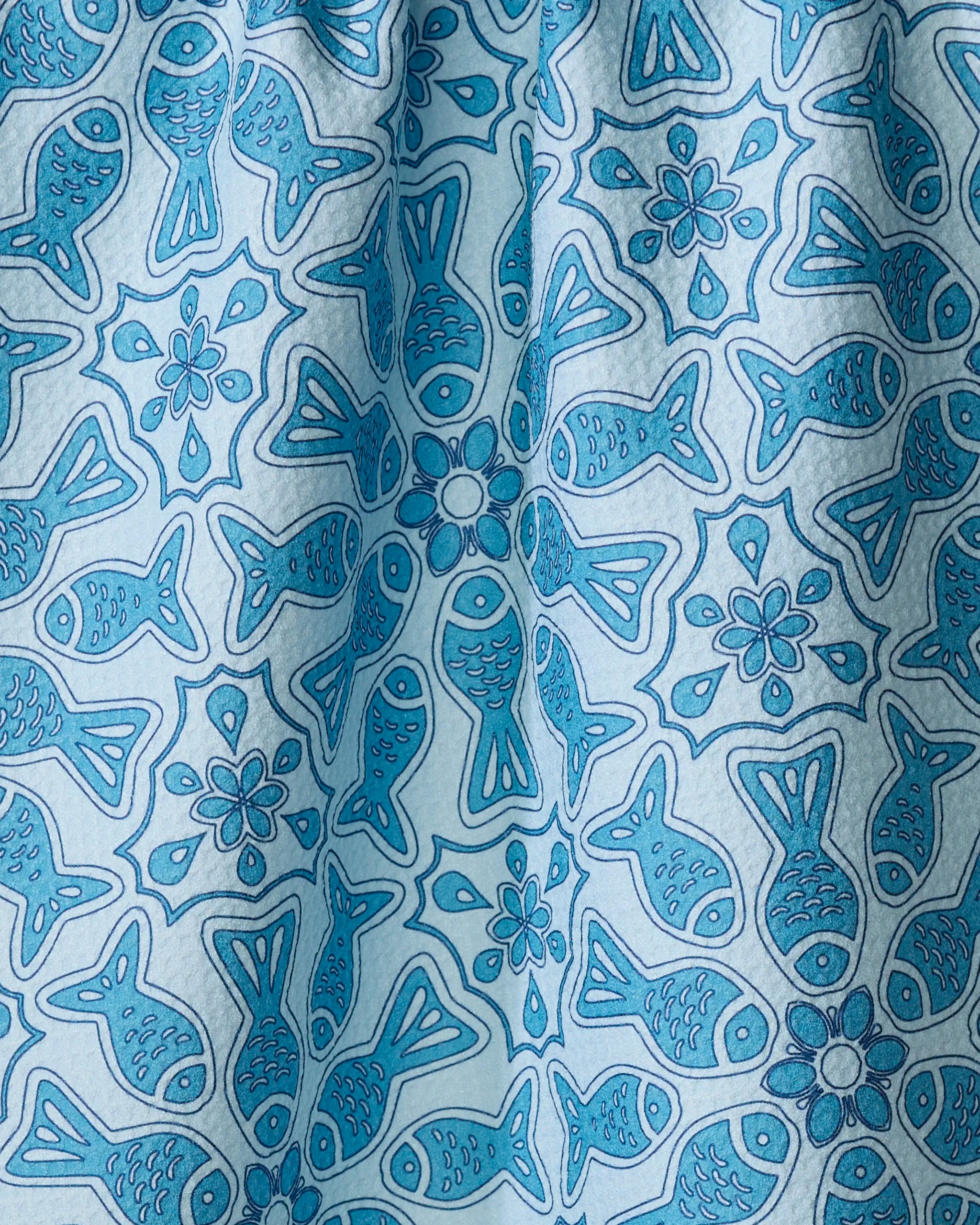 The Little Fish Mandala tea towel by Marta Harvey features blue fish and flower motifs on a light blue background, with soft folds and subtle texture. Made from recycled materials, it's an eco-friendly addition to your kitchen.