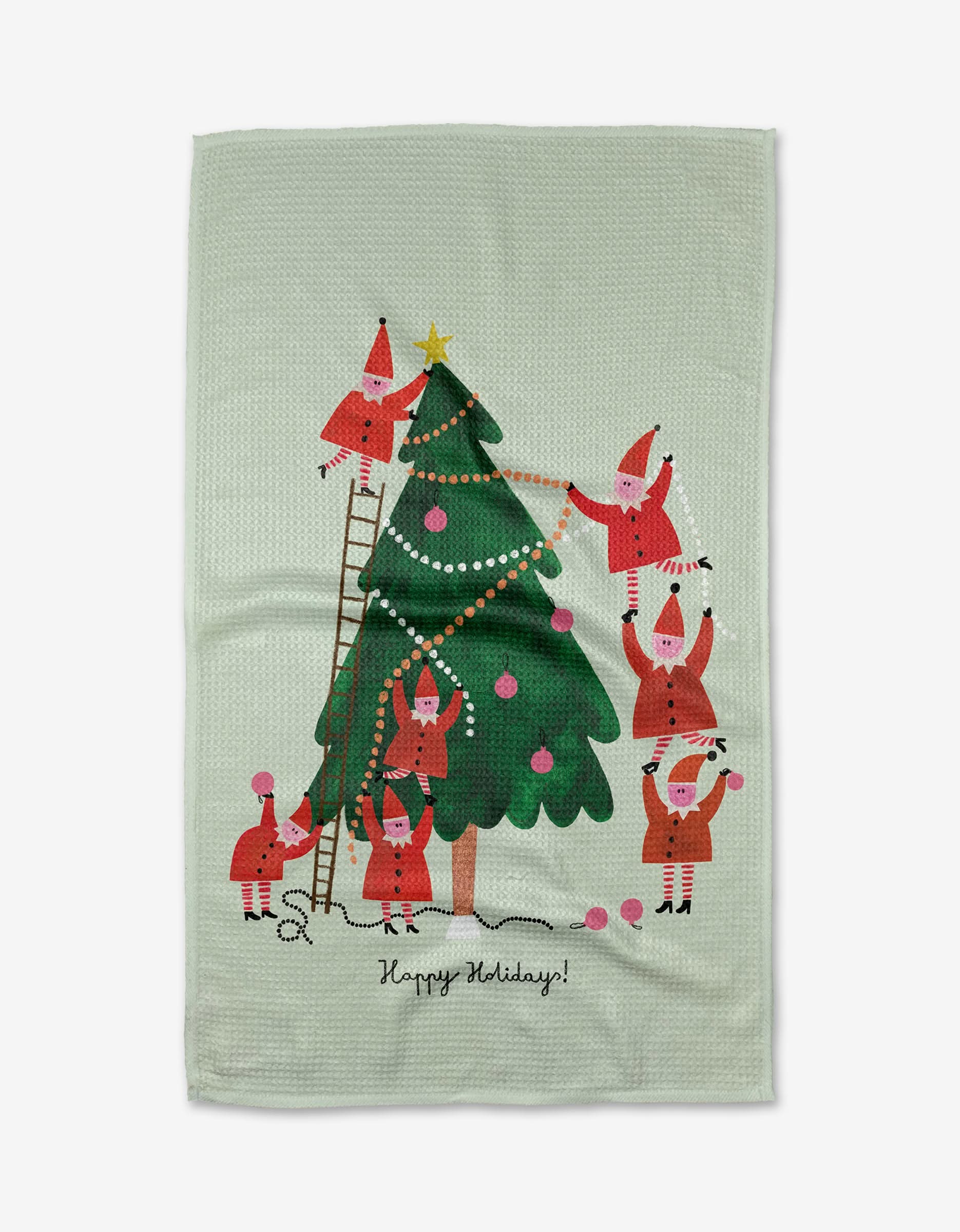 The Little Helpers kitchen towel by Daria Solak features cartoon Santas decorating a tree with ornaments and garland, using a ladder and forming a pyramid. Happy Holidays! is written at the bottom. Eco-friendly and festive!.