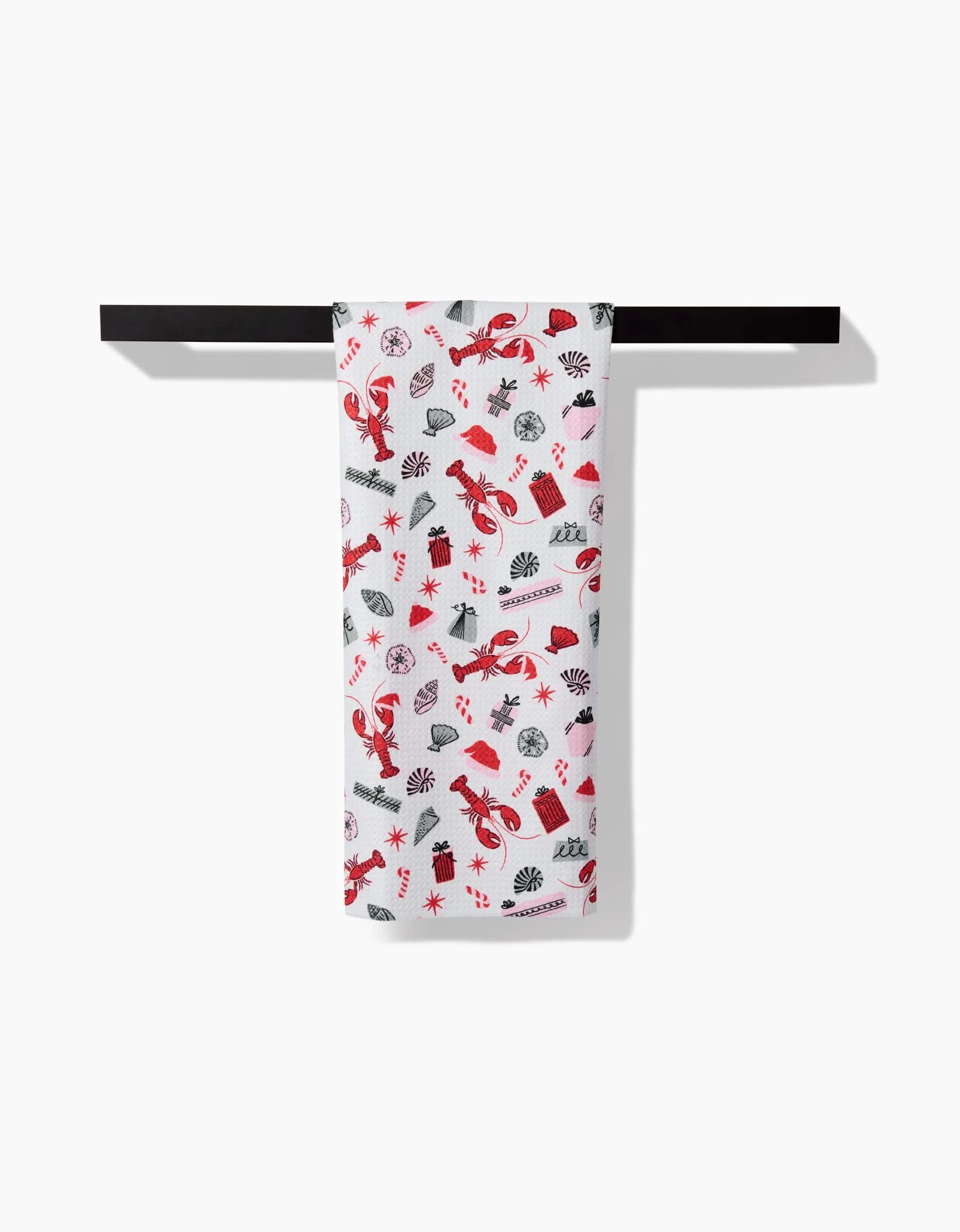 A Lobster Holiday tea towel by Charlie Rowan Designs, featuring red and black lobster and sea-themed prints, hangs neatly over a black towel bar against a plain white background.