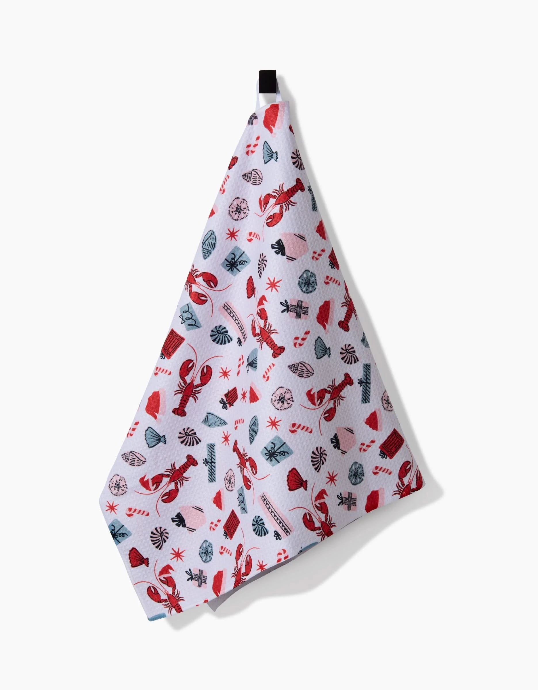 The Lobster Holiday tea towel by Charlie Rowan Designs features ultra-absorbent white fabric with a colorful nautical pattern of red lobsters, seashells, and starfish. It hangs from a black loop against a white background.