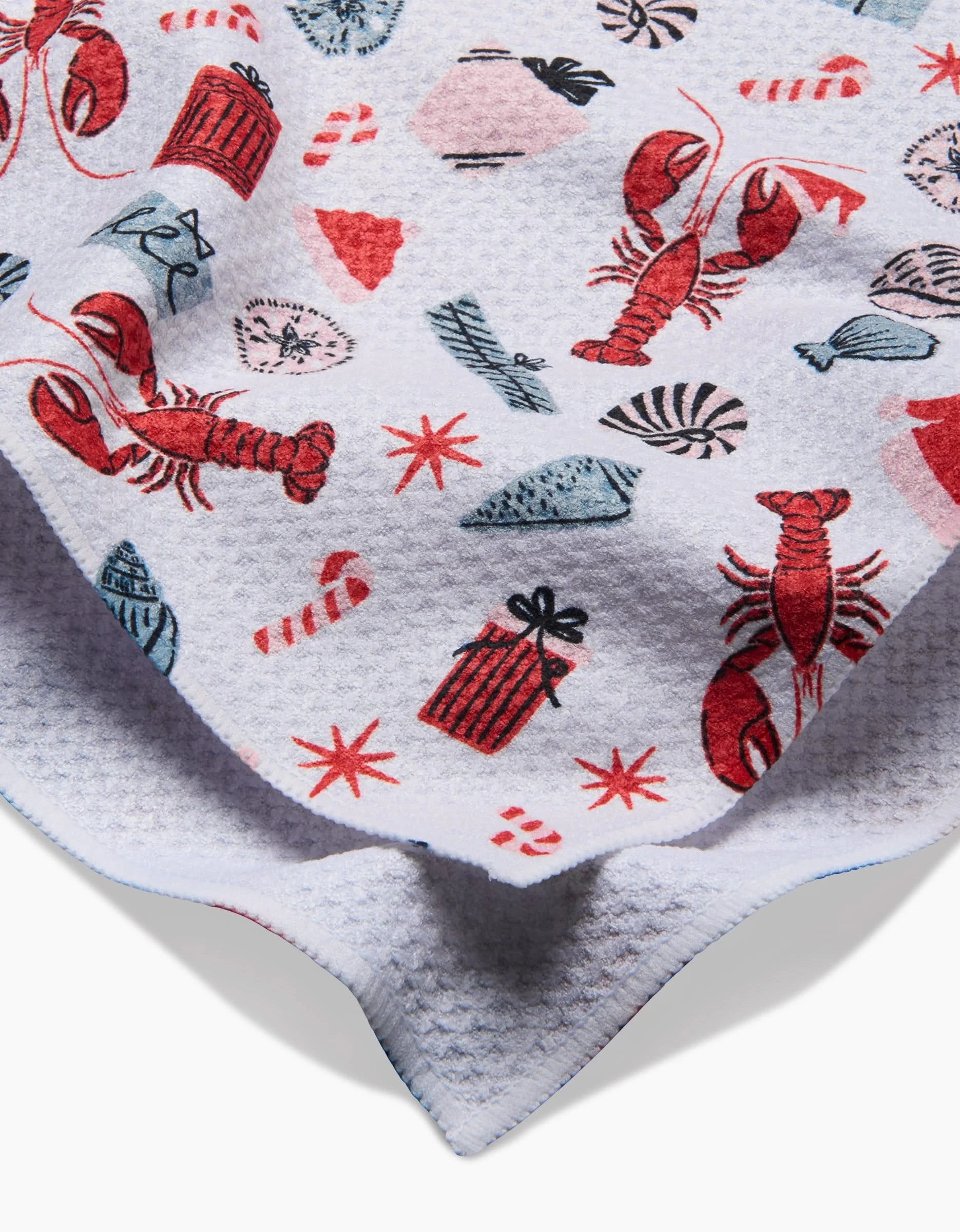 The Lobster Holiday tea towel by Charlie Rowan Designs features playful red lobsters, seashells, gifts, candy canes, and stars—a festive blend of coastal and holiday themes. Ultra-absorbent and stylish, it’s perfect for any kitchen.