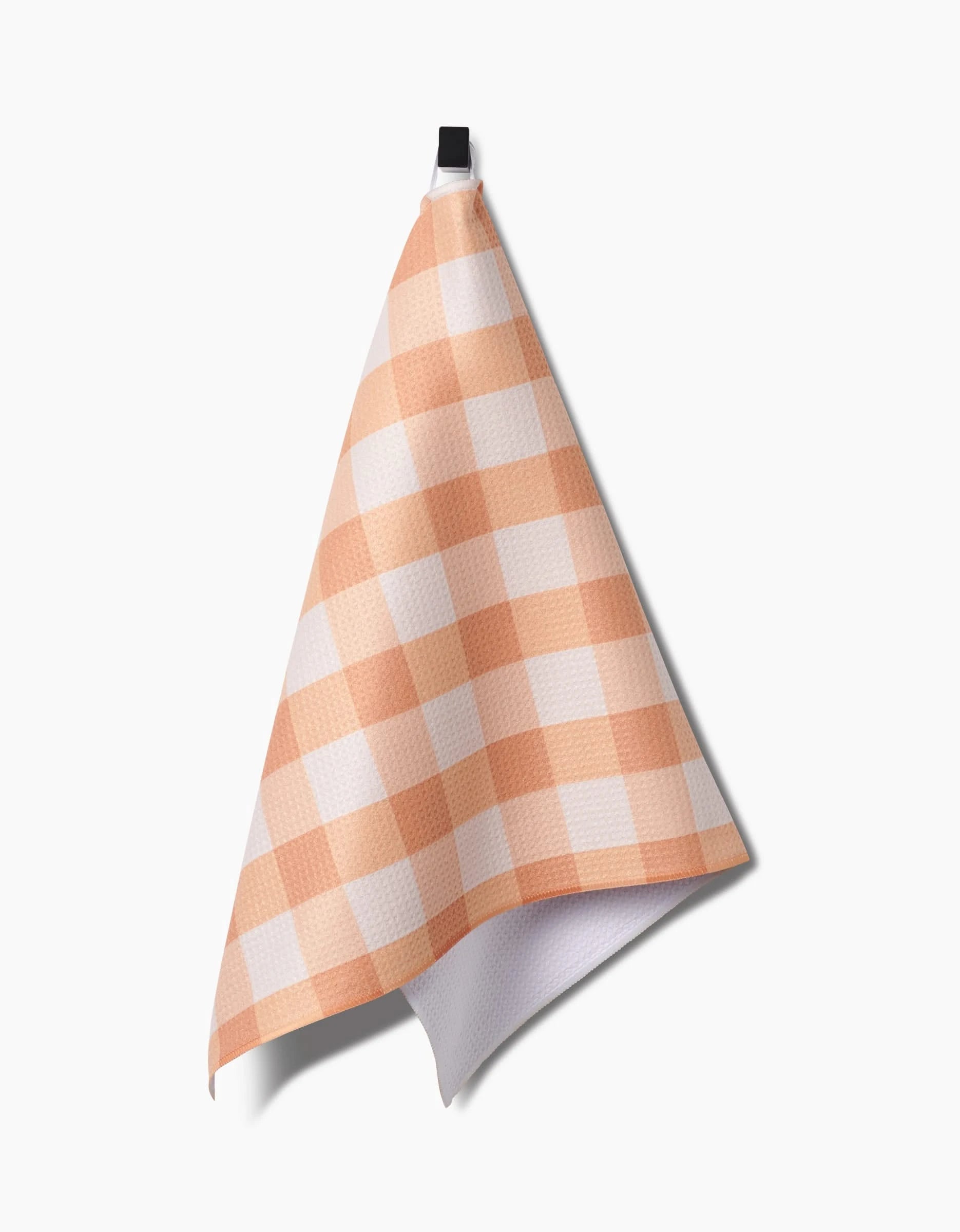 The Lorraine tea towel by Kelsi Fullmer, featuring a peach and white checkered design and made from recycled materials, hangs from a black loop against a plain white background.