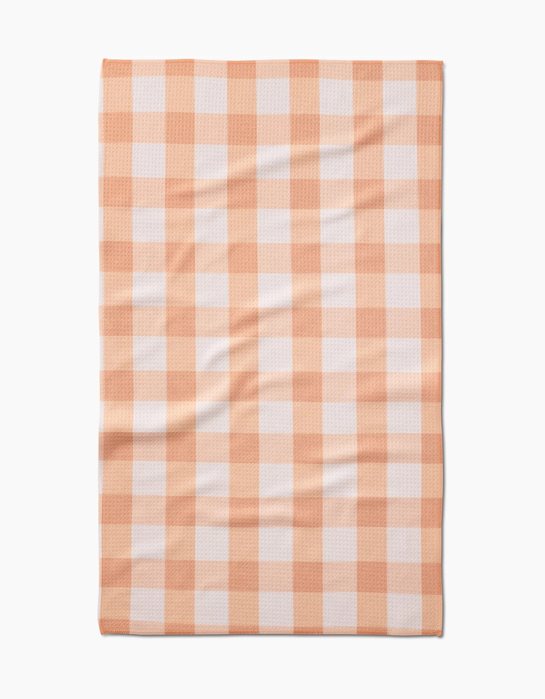 The Lorraine tea towel by Kelsi Fullmer is a rectangular Geoweave fabric towel made from recycled materials, shown flat with slight wrinkles and featuring a peach and white gingham checkered pattern.