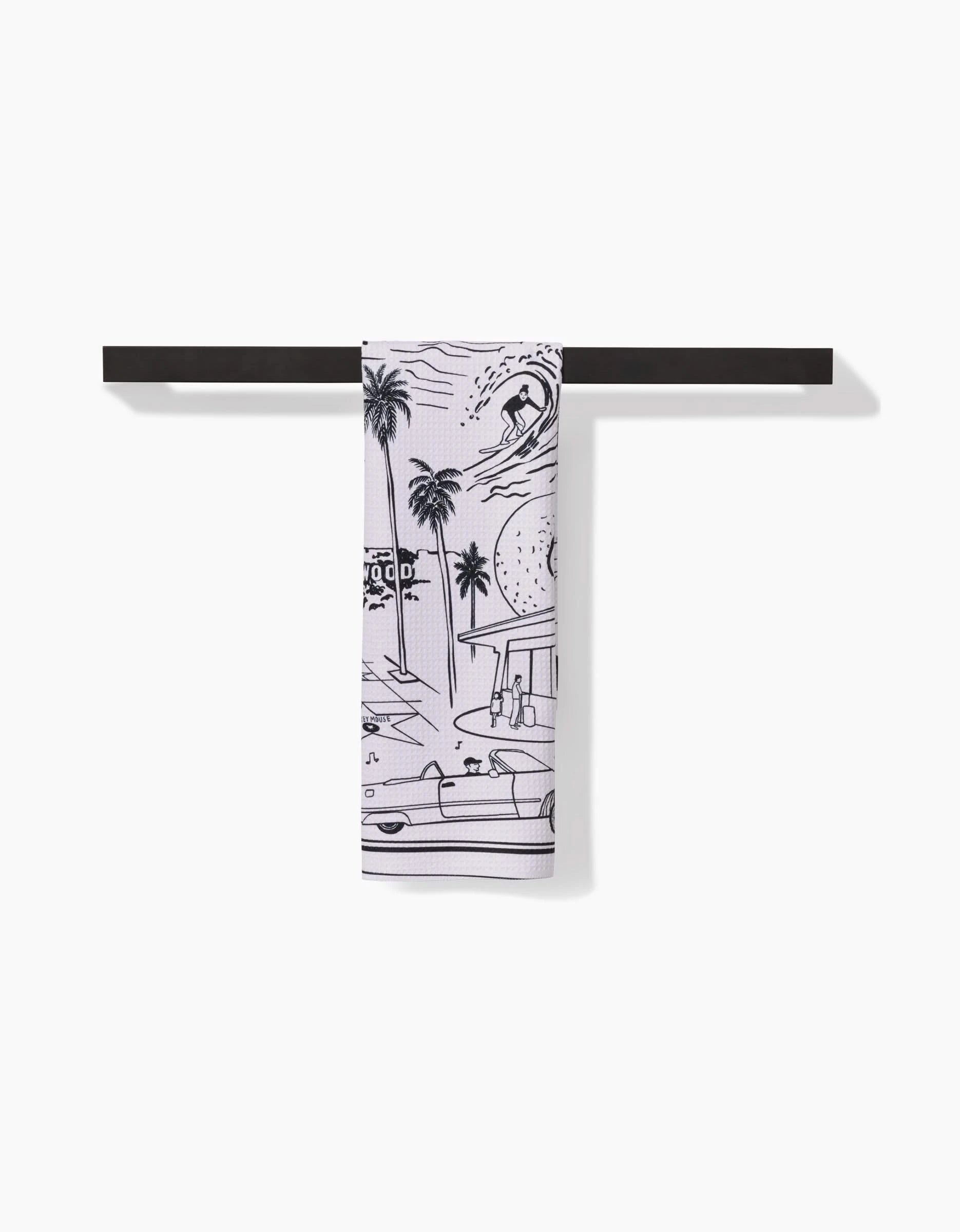 The Elisabeth Wing Los Angeles tea towel, crafted from white Geoweave™ fabric and featuring black line art of a beach scene, hangs neatly on a minimalist black towel bar against a white background.