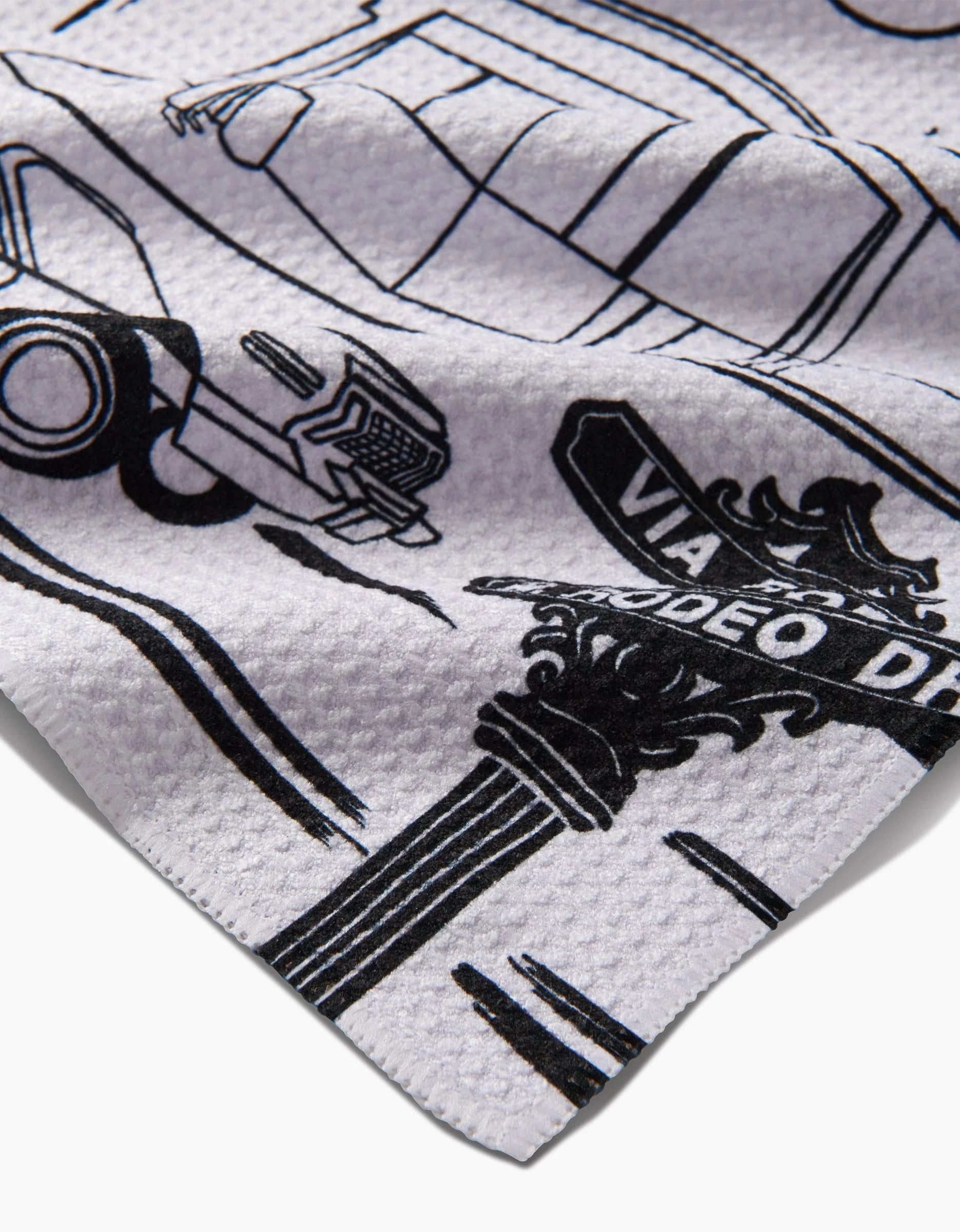 A close-up of the Los Angeles tea towel by Elisabeth Wing, made from white Geoweave™ fabric and featuring black line art of a vintage car and a VIA RODEO DRIVE street sign.
