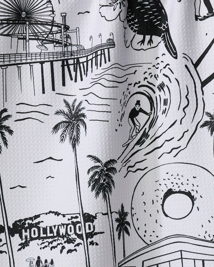 This absorbent dish towel by Elisabeth Wing, named "Los Angeles," features a black-and-white illustration of a surfer, palm trees, a pier ferris wheel, the Hollywood sign, and a donut—iconic scenes from California.