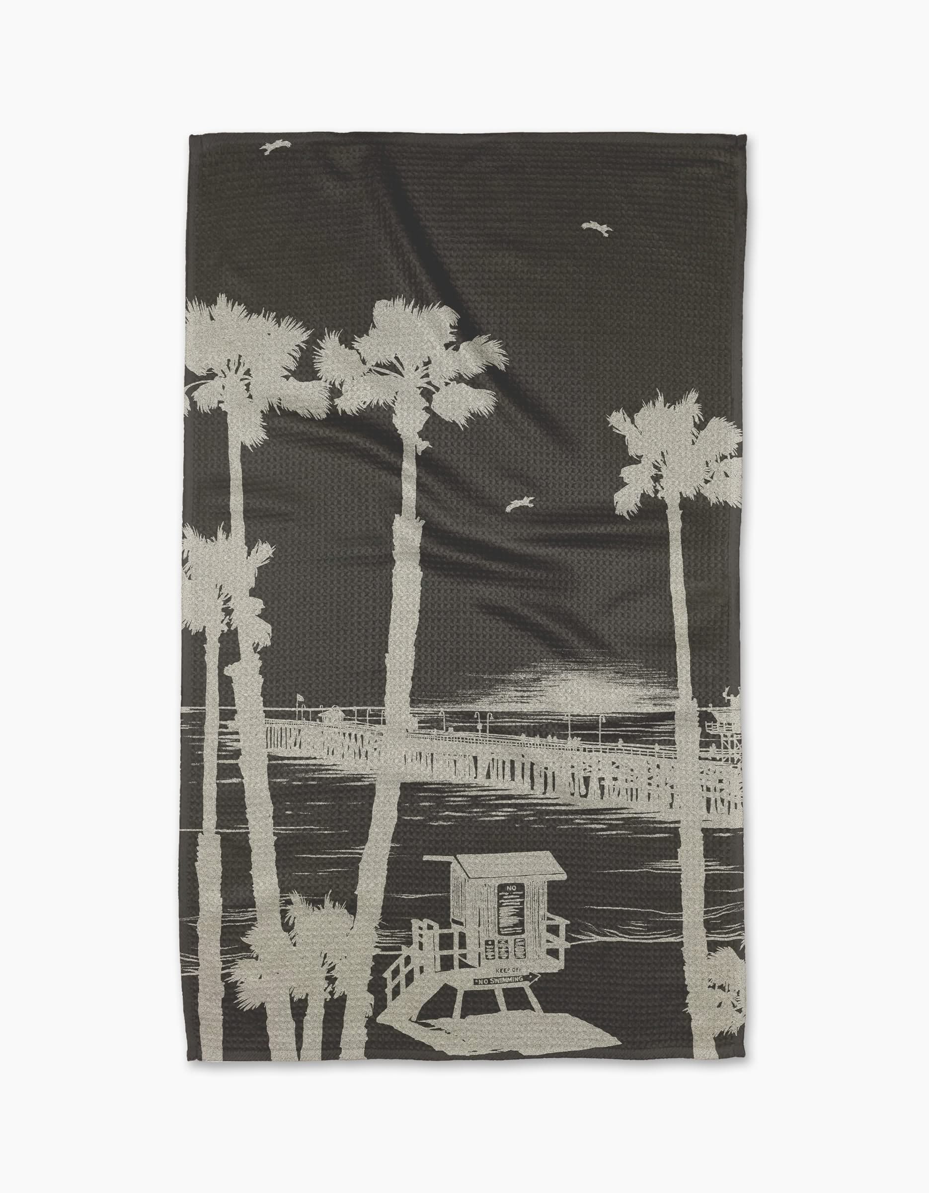 The Geometry Lost In Clemente blanket showcases a beige sketch of palm trees, a pier, and birds on a dark background, crafted from ultra-absorbent Geoweave fabric for comfort and style.