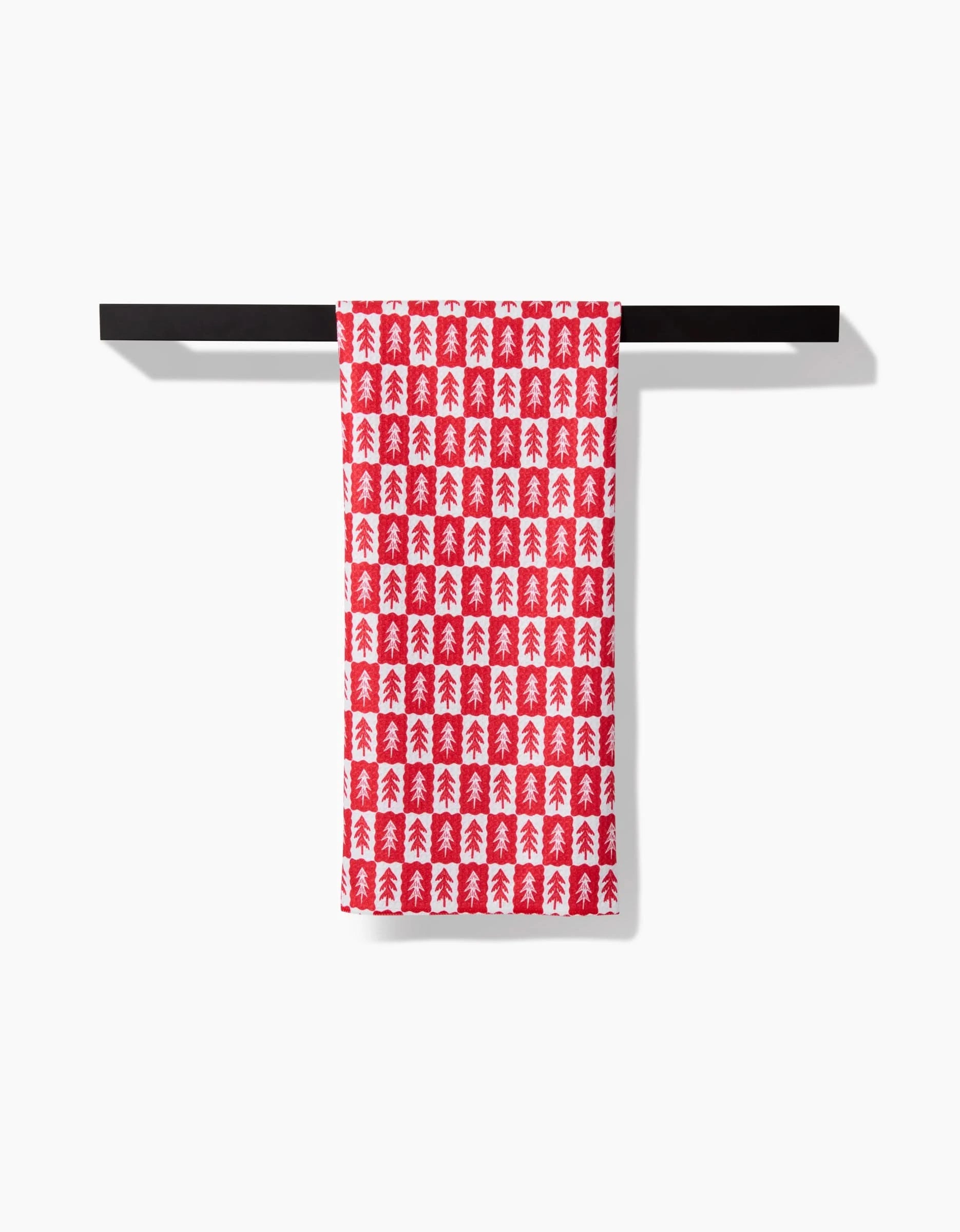 The Louis Pines tea towel by Roxy Marj, featuring a red Christmas tree pattern on ultra-absorbent white fabric, hangs neatly on a black towel bar against a plain white background.