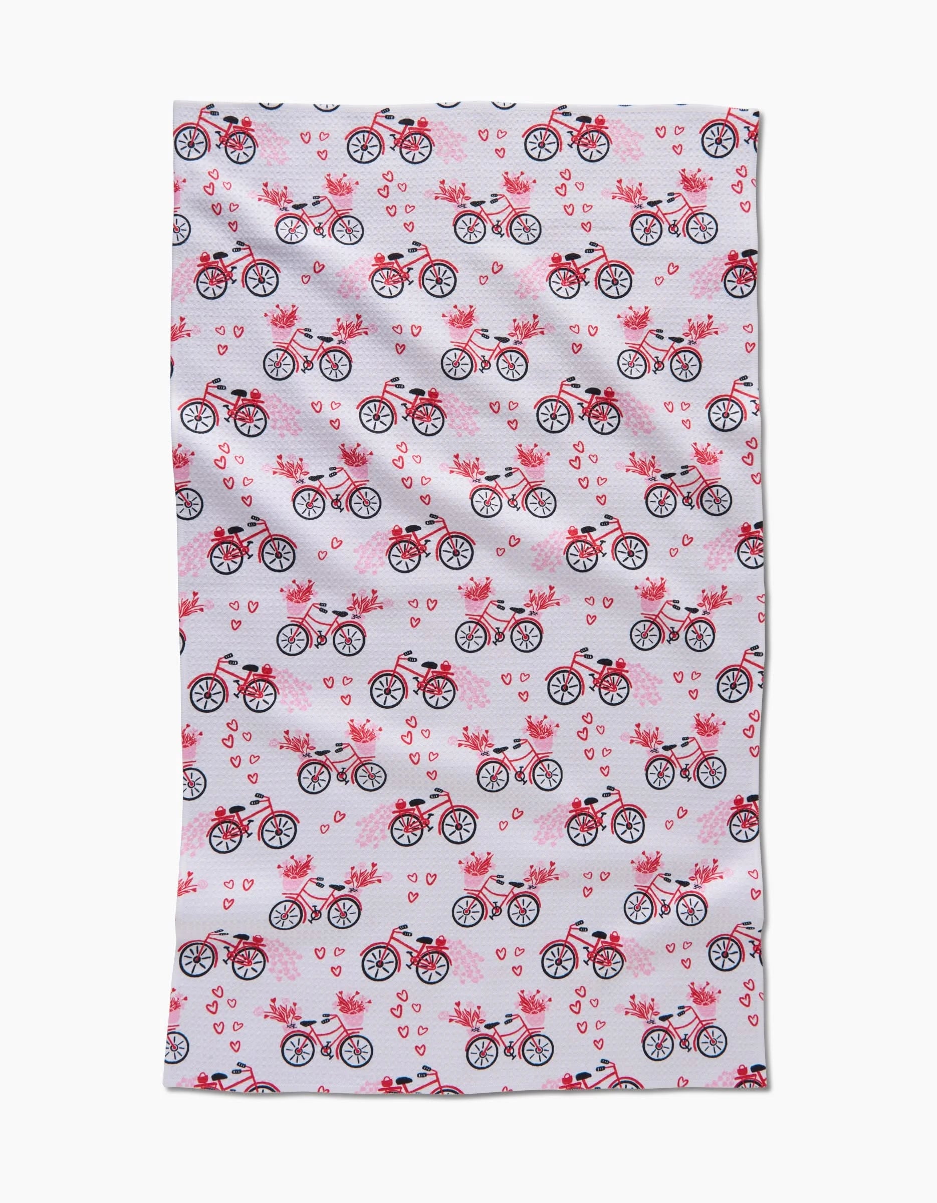 The Love Bikes tea towel by Charlie Rowan Designs features black and pink bicycles with flower-filled baskets, pink hearts, and birds. This quick-drying towel adds a charming touch to any kitchen.