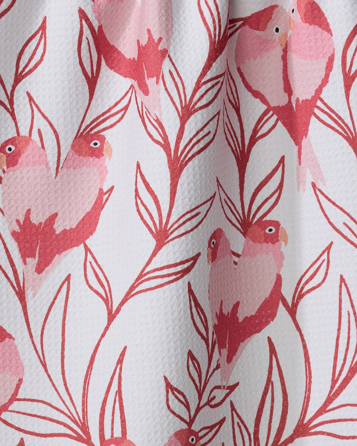 The Love Birds tea towel by Hufton Studio features pink and red birds with heart-shaped bodies perched on leafy branches, all set against a white textured background—a charming, recycled kitchen accessory.