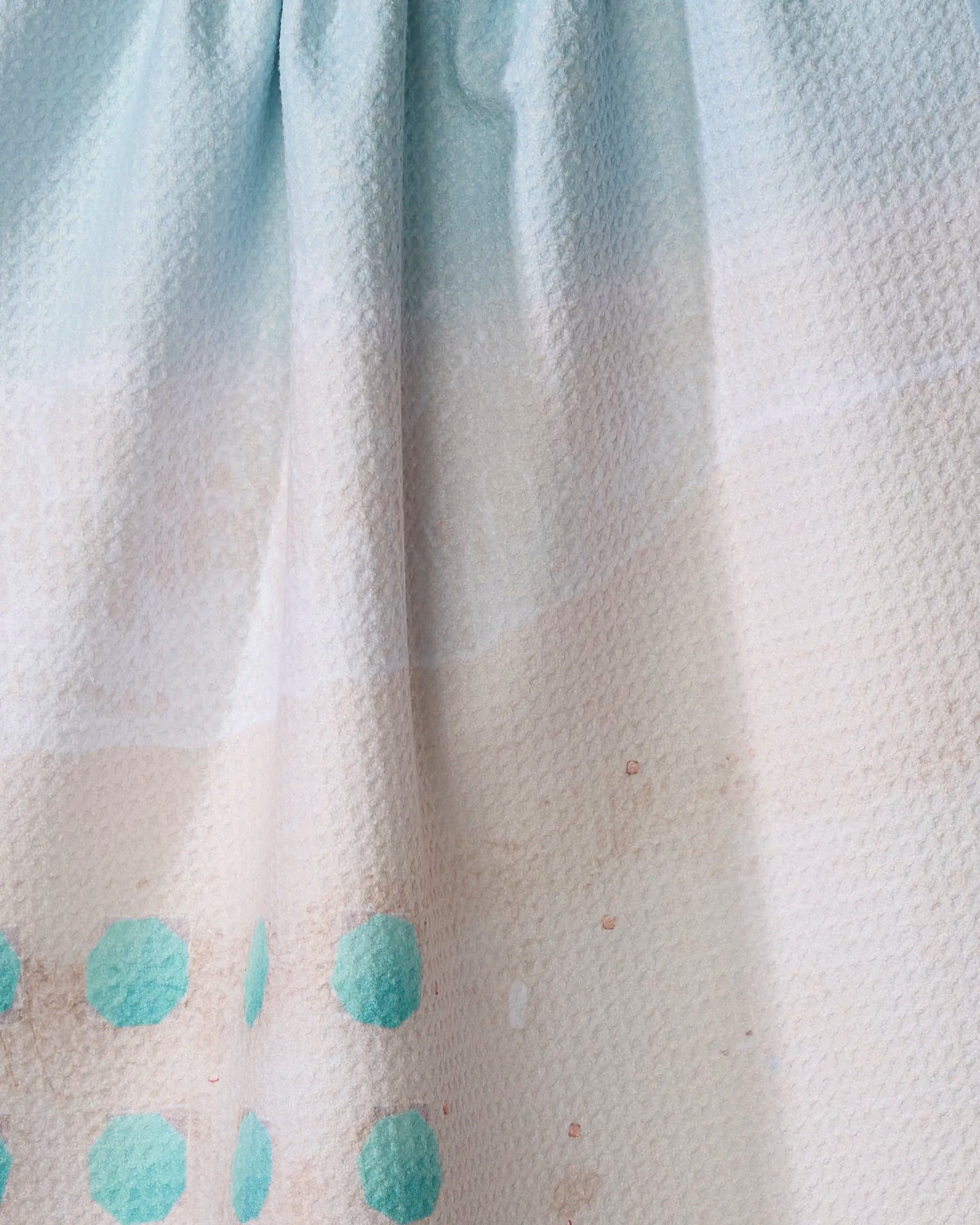 The Love From Hawaii dish towel by Kait Hanson features a textured fabric with a blue-to-cream gradient and turquoise polka dots along the lower edge. Absorbent and stylish, it has a slightly gathered top for added charm.