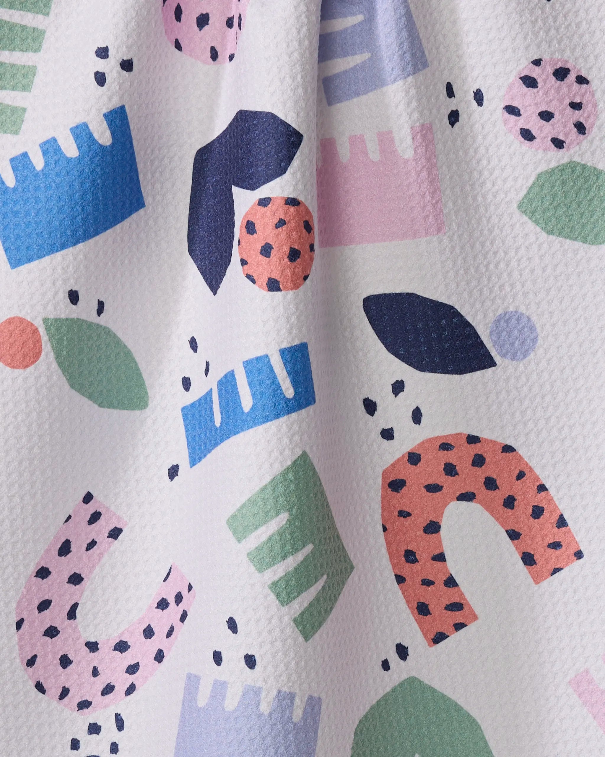 The Claire Iglesias "Love Letters" tea towel is textured, made from recycled materials, and adorned with colorful abstract shapes—arches, leaves, and dots in pink, blue, green, navy, purple—with bold black speckles.