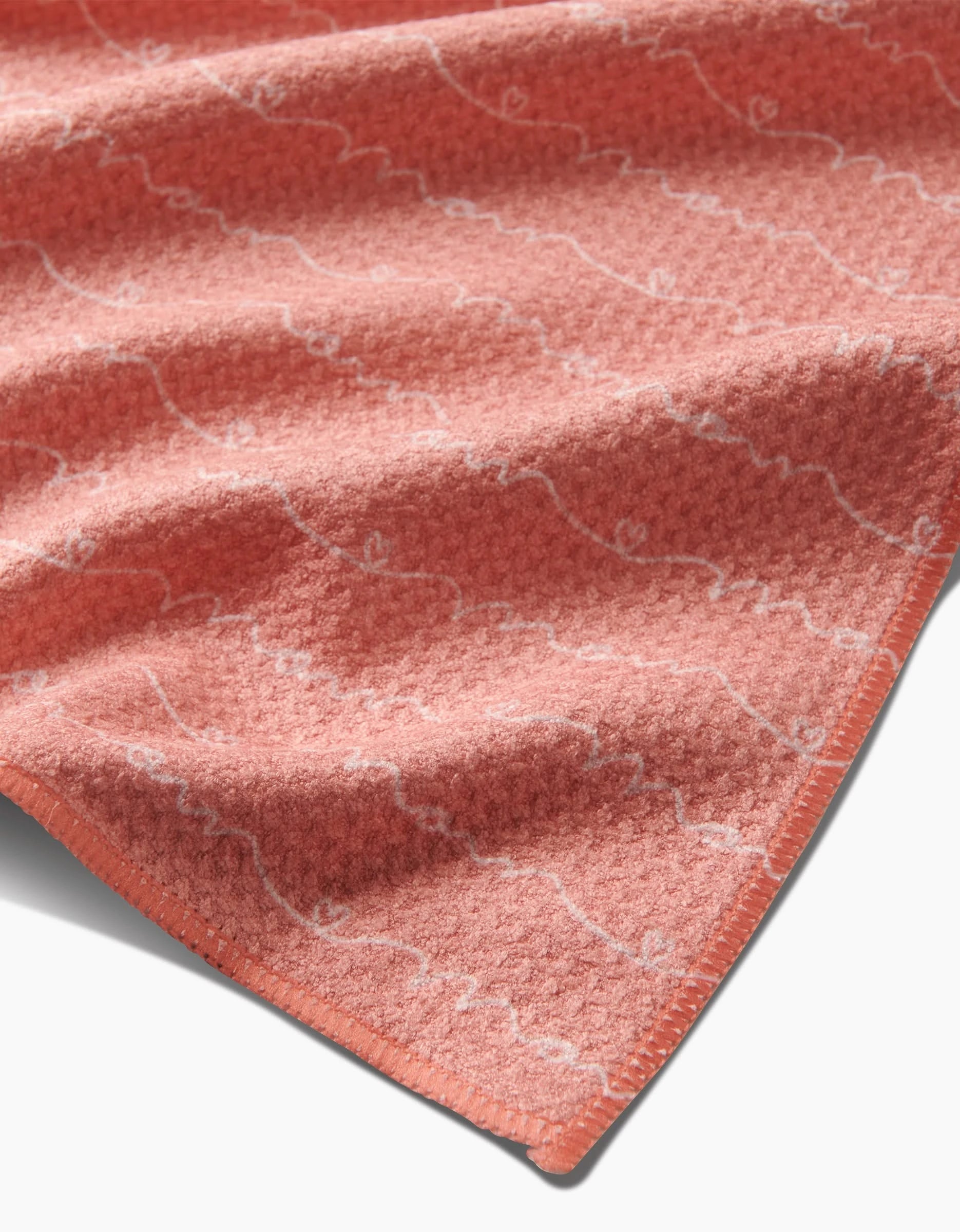 A close-up of the Sarah Reed Love of Mom blanket, crafted from soft Geoweave™ fabric in coral with a subtle white wavy pattern and neatly finished edges.