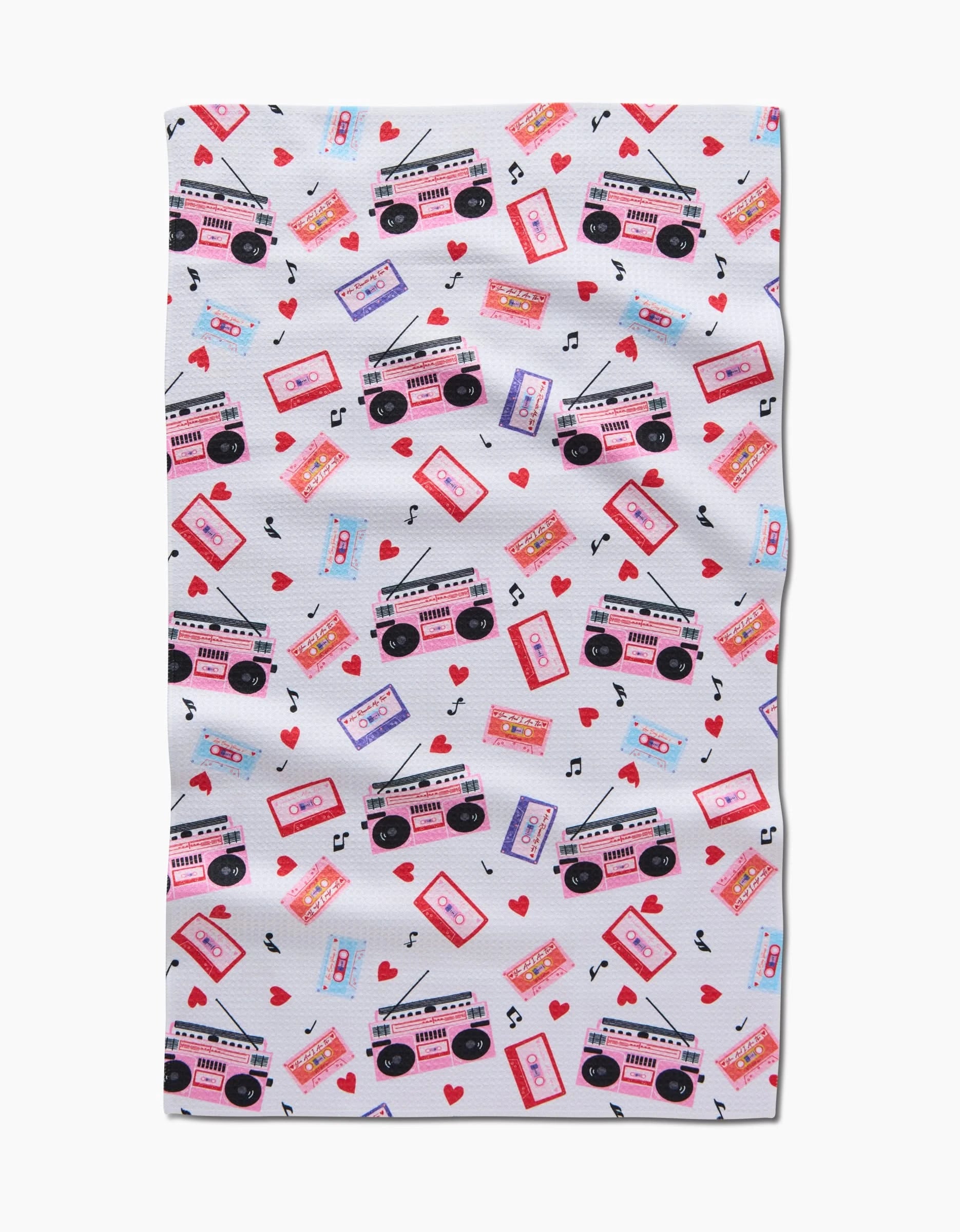 The Love Playlist tea towel by Vaishali Design Studio showcases pink and purple cassette tapes, boomboxes, red hearts, and black musical notes in a lively scattered pattern on white.