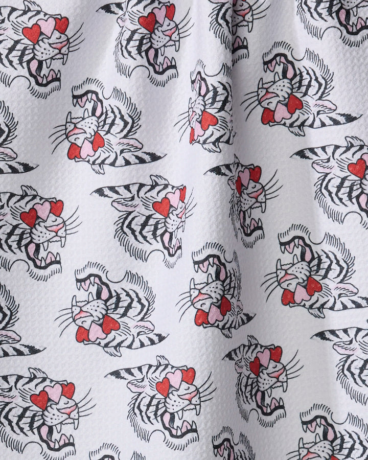 The Cole Strem Love Tiger tea towel features white fabric with a repeating cartoon tiger pattern—heart-shaped eyes, red noses, and snarling faces. Ultra-absorbent and made from recycled materials, it has a slightly dimpled texture.