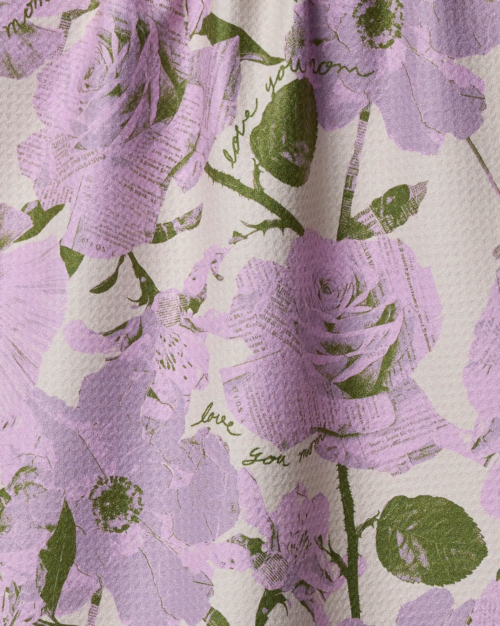 The Geometry “Love U Forever” tea towel features a textured, eco-friendly design with large lilac and green flowers over subtle script and text that says “love you mom” in green.