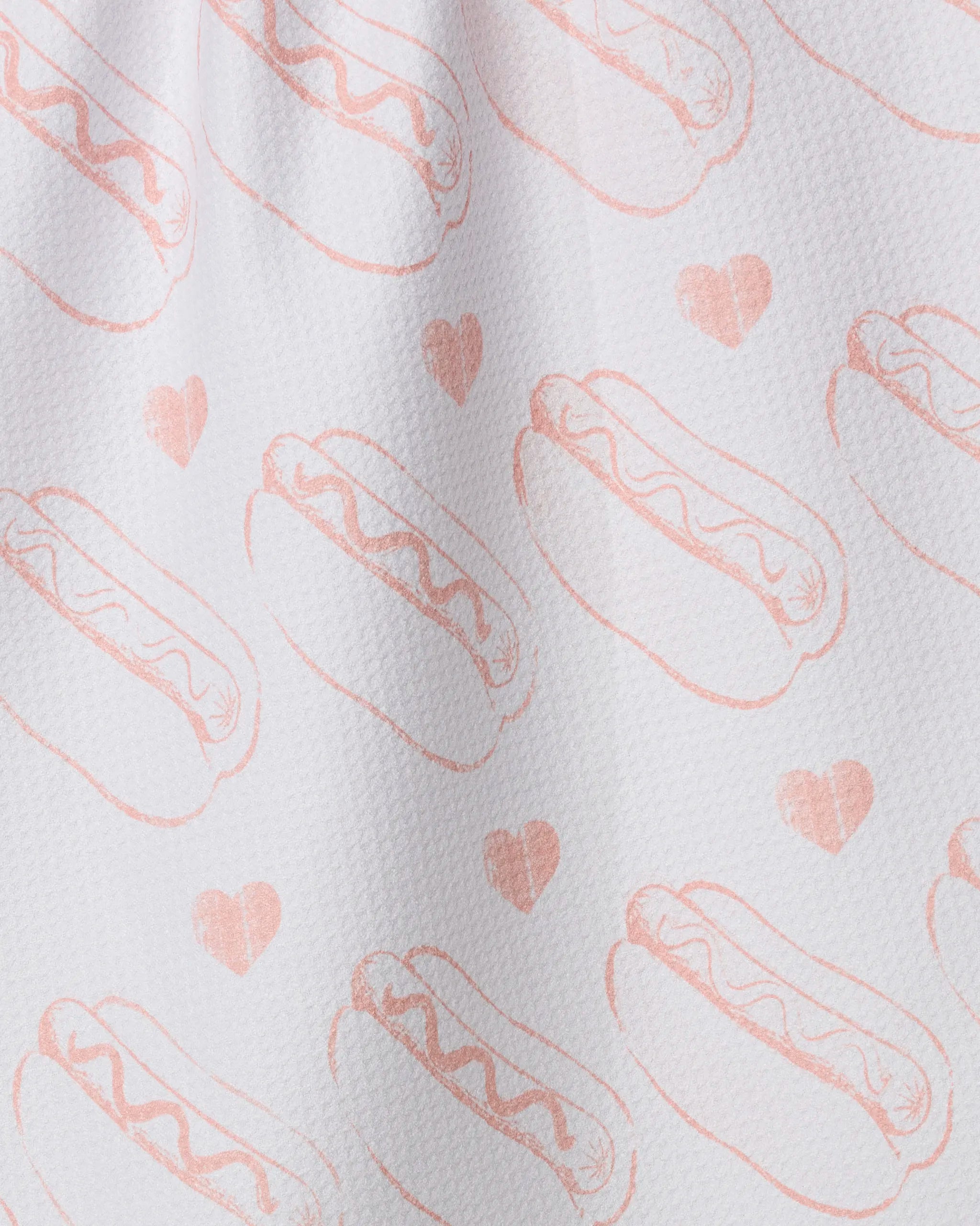 Lovely Franks by Geometry is a white textured recycled kitchen towel adorned with a repeating pattern of light pink hot dog illustrations and scattered small hearts.
