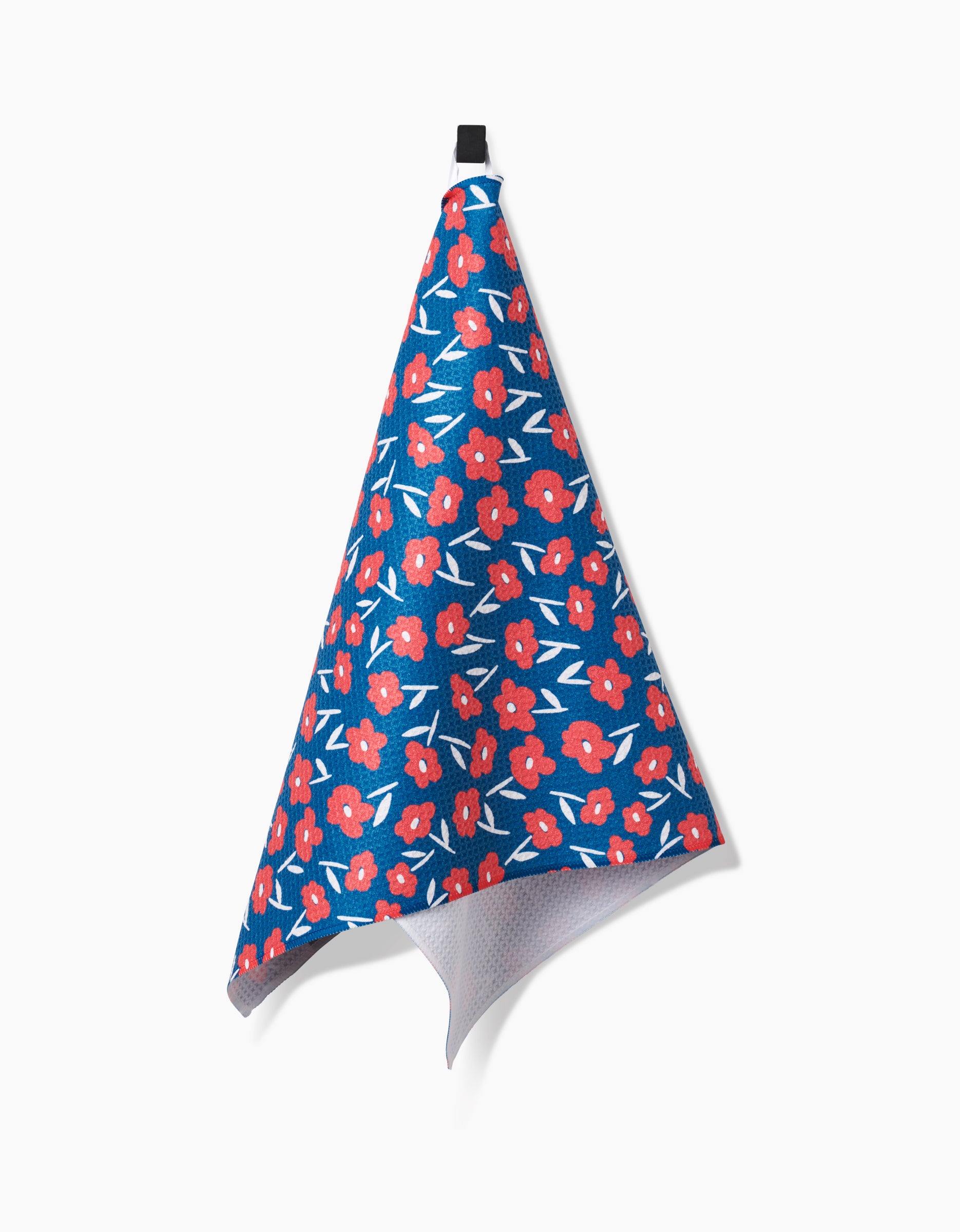 The Hufton Studio Luca Daisy Red tea towel, featuring a red and white floral pattern on blue Geoweave fabric with a light gray underside, hangs by a black loop against a plain white background.