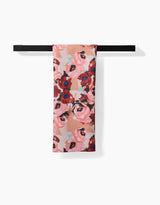 The Lucia Tea Towel by Ania Zwara Art features pink and red roses with green leaves, hanging over a black towel bar. Made from Geoweave™ fabric, it offers enhanced softness and durability against a white background.