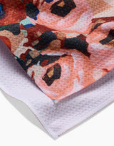 A close-up of the Lucia Tea Towel by Ania Zwara Art, made from recycled materials, featuring a textured white underside and a vibrant abstract floral pattern in pink, red, black, and blue on top.