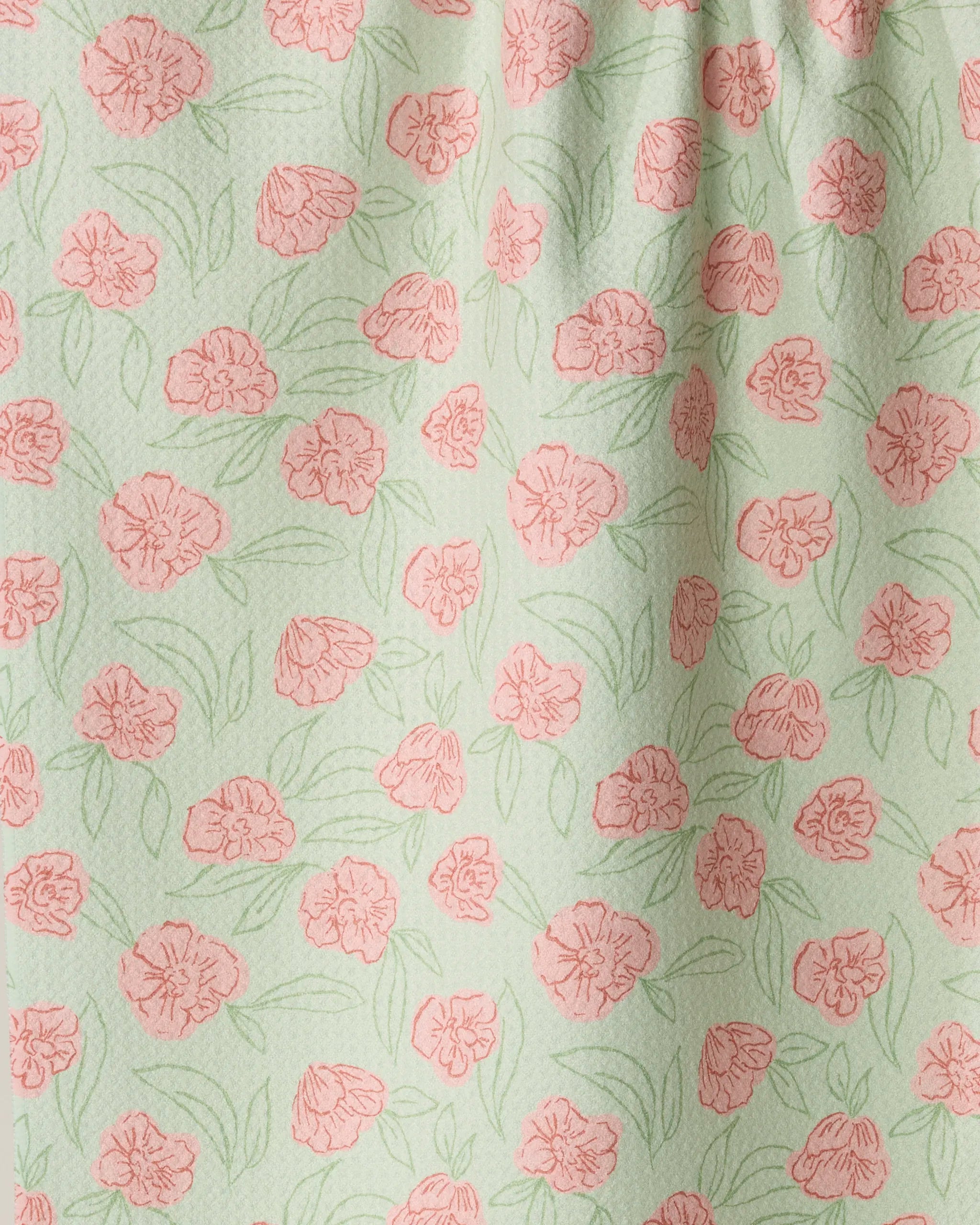 Introducing Lucky Bloom by Geometry: a light green towel adorned with a repeating pattern of pink flowers and green leaves, creating a soft, delicate, spring-inspired design. Crafted from recycled materials, this absorbent and quick-drying kitchen tea towel features gentle fabric folds—perfect for everyday use.