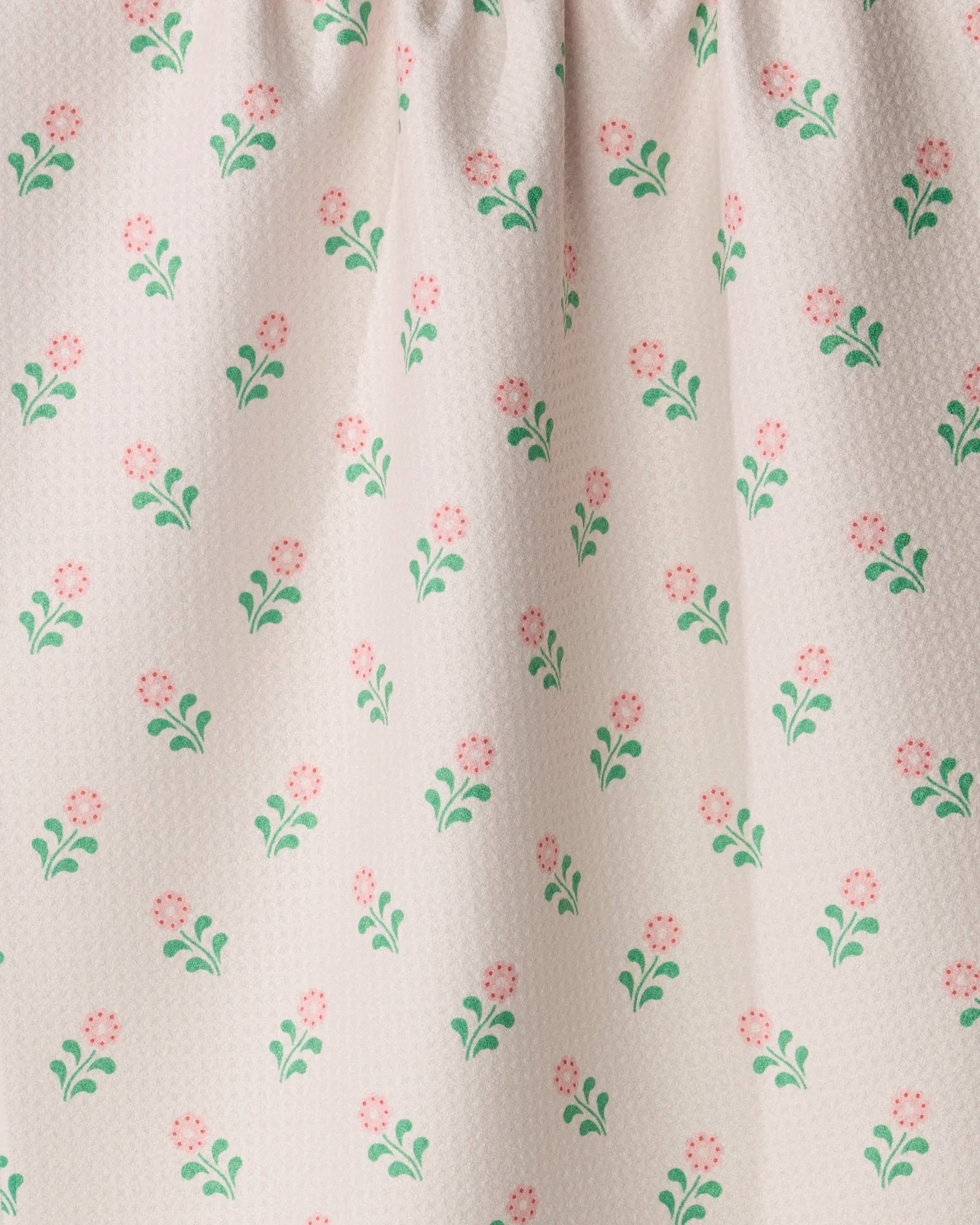 Lucky Blossom by Geometry features white textured fabric adorned with a repeating pattern of small pink flowers and green leaves. The gathered top creates gentle folds, making it an ideal choice for a charming tea or kitchen towel crafted from recycled materials.