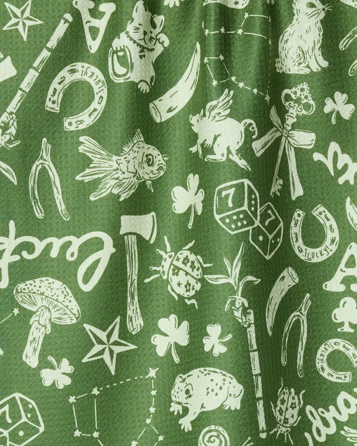 The Geometry Lucky Draw Symbols tea towel features white lucky motifs—horseshoes, clovers, dice, and more—on green quick-drying recycled fabric.