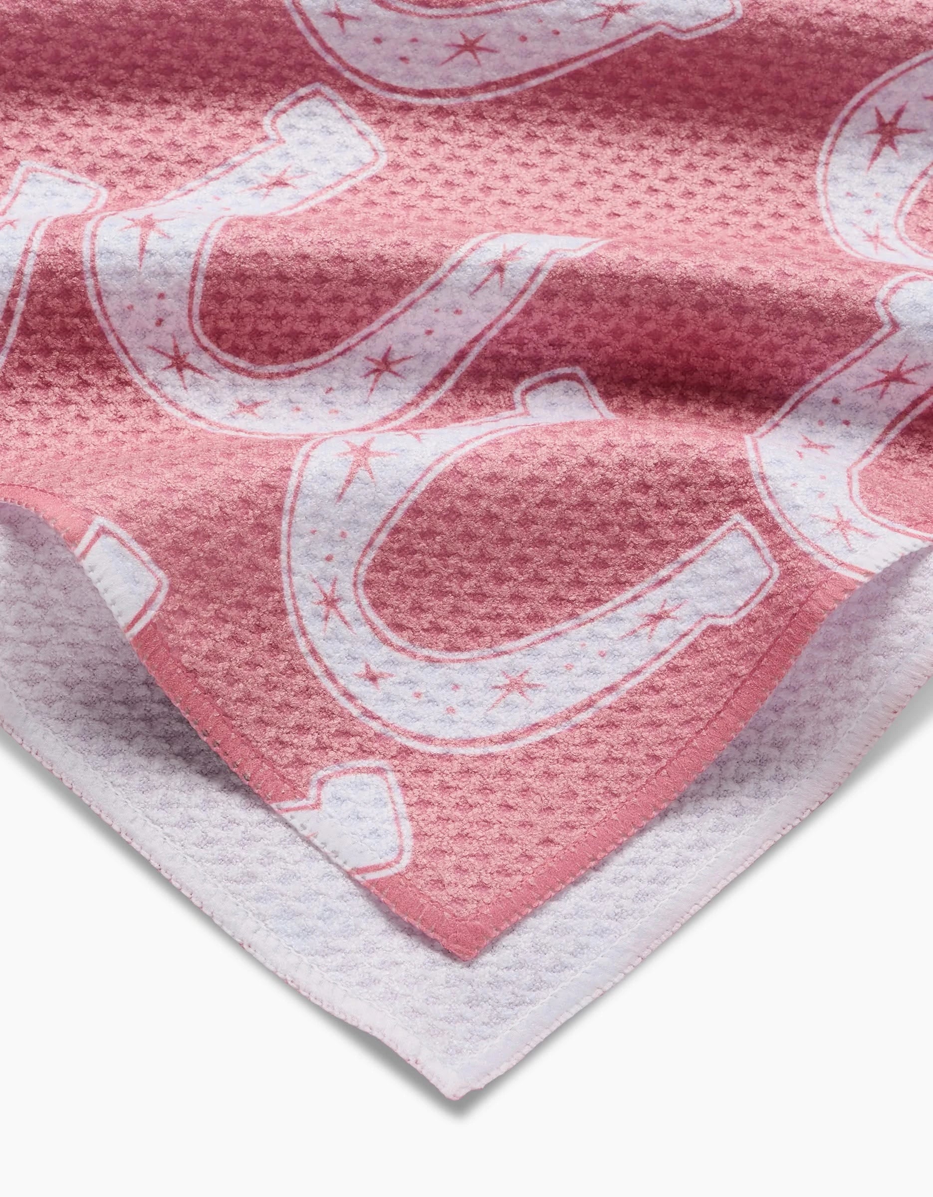 Aubrey Fairchild’s Lucky Horseshoe tea towel is made from recycled materials, featuring a textured pink fabric with a white border and large white horseshoes outlined in red.