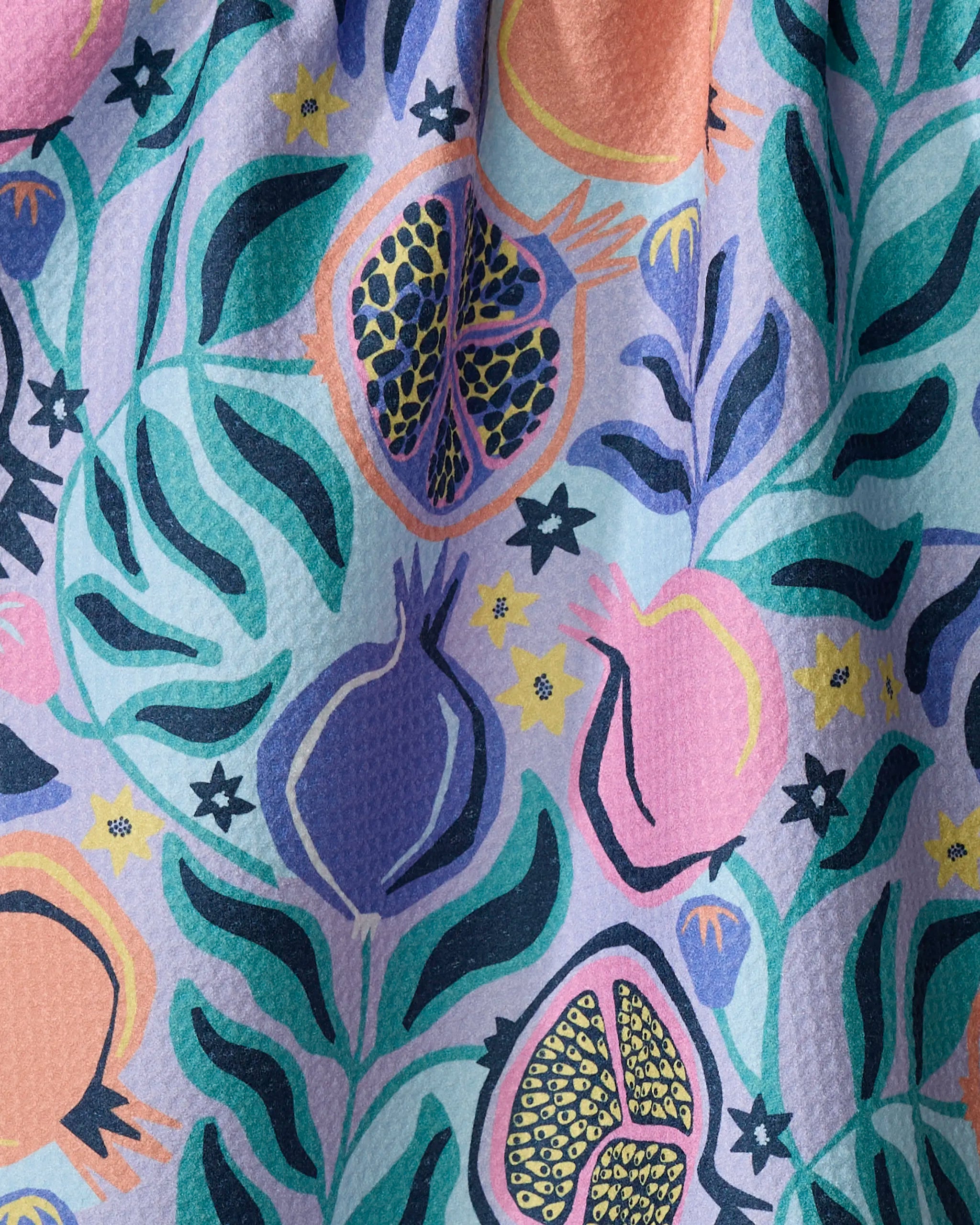 The Lucky Pomegranate kitchen towel by Masha Volnova features a lively, stylized pomegranate and leaves pattern in vibrant purple, pink, teal, green, and yellow on textured recycled fabric.