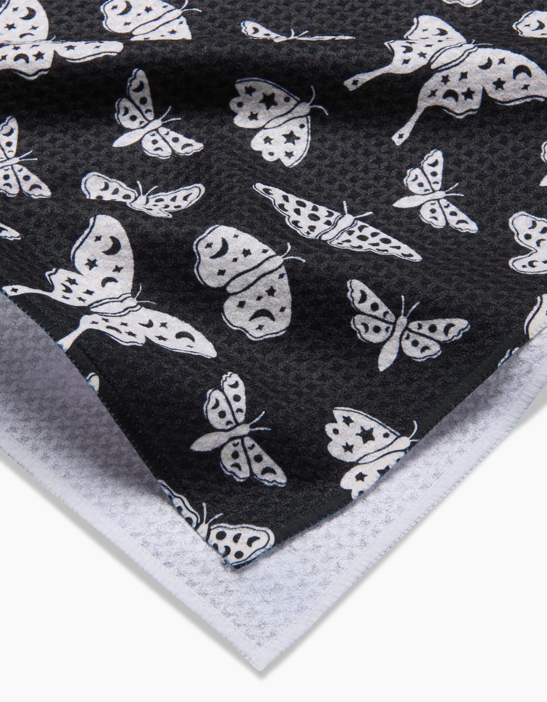 A close-up of Kayla Ann’s Lunar Moths Black fabric, featuring a white moth pattern on black, layered over a textured recycled white kitchen towel.