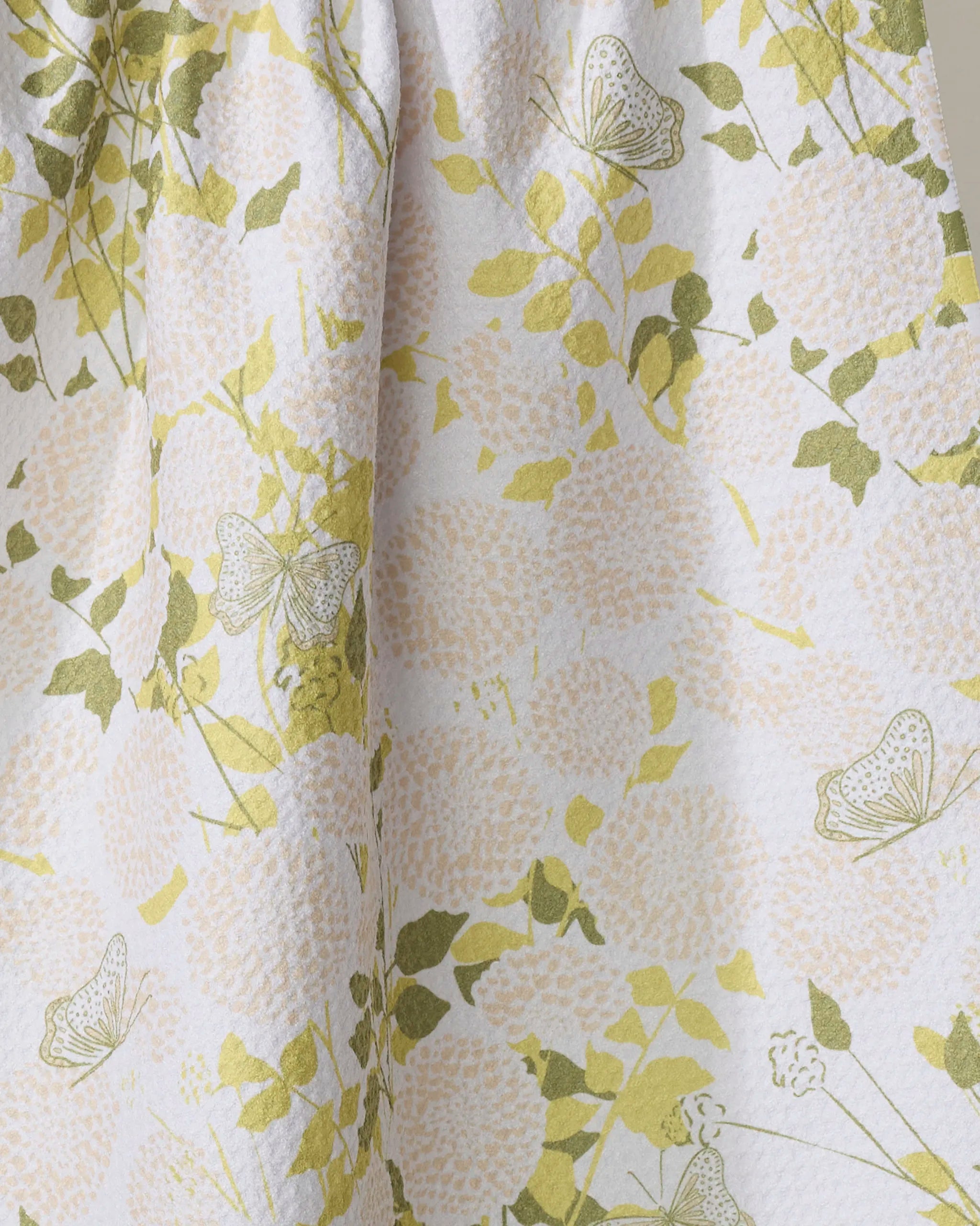 A close-up of the Lush Garden kitchen tea towel by Second Nature Studio, featuring pale pink flowers, green leaves, and delicate butterflies on a textured white background—ideal for brightening your kitchen.