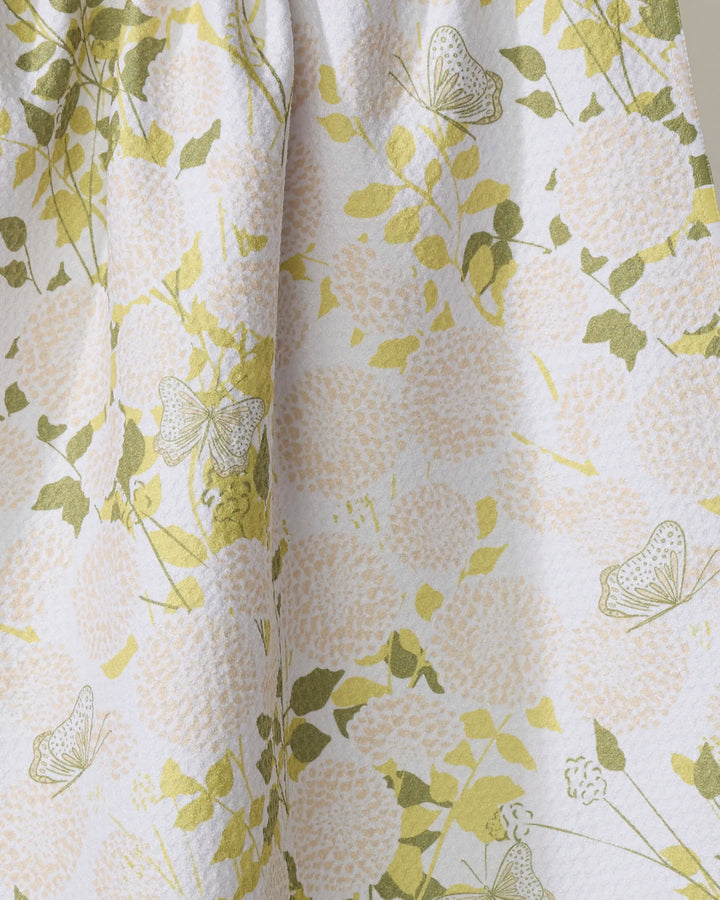 A close-up of the Lush Garden kitchen tea towel by Second Nature Studio, featuring pale pink flowers, green leaves, and delicate butterflies on a textured white background—ideal for brightening your kitchen.