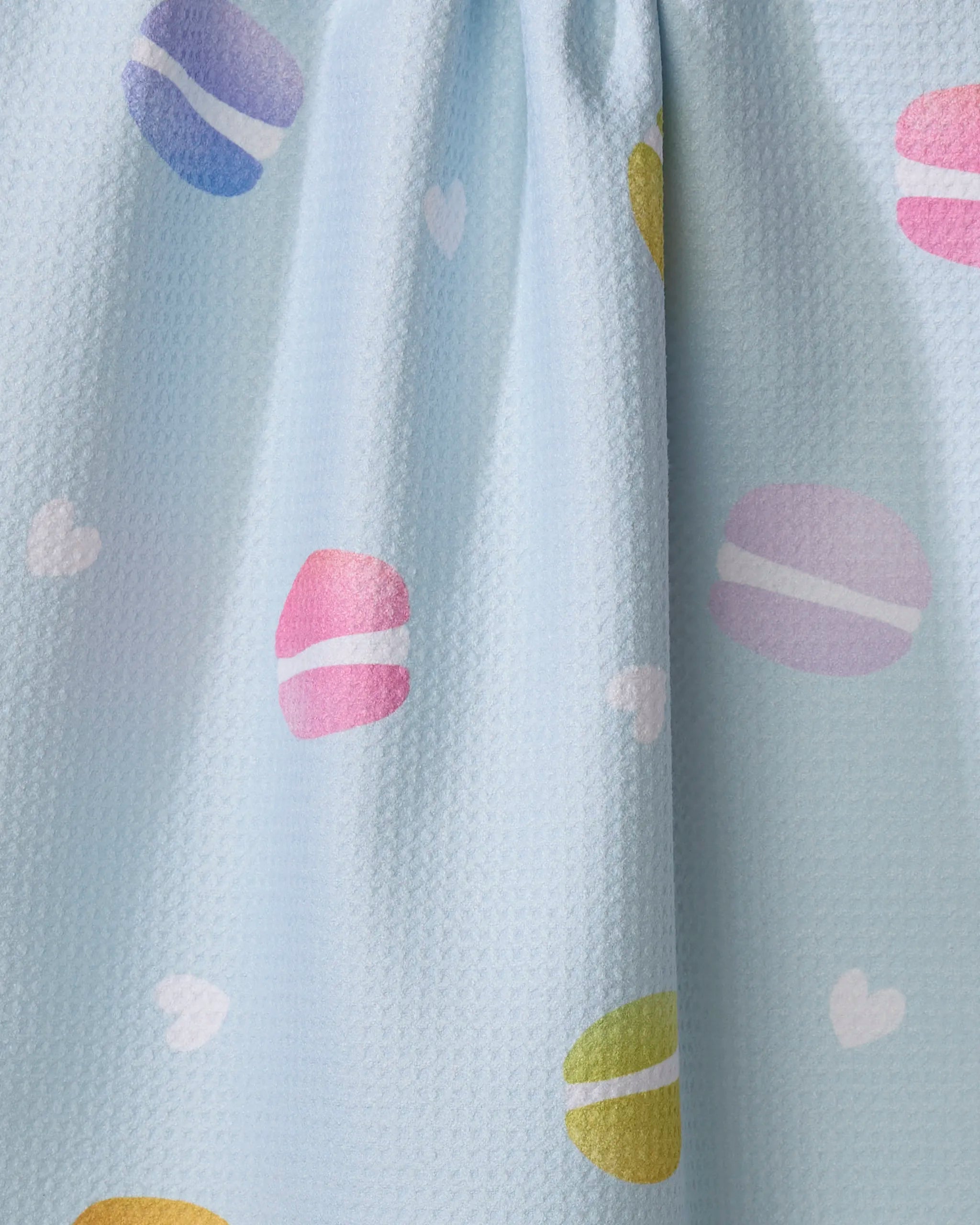 The Mac Flip by Nora's Macarons is a light blue, ultra-absorbent towel adorned with pastel macaron patterns and small white hearts.