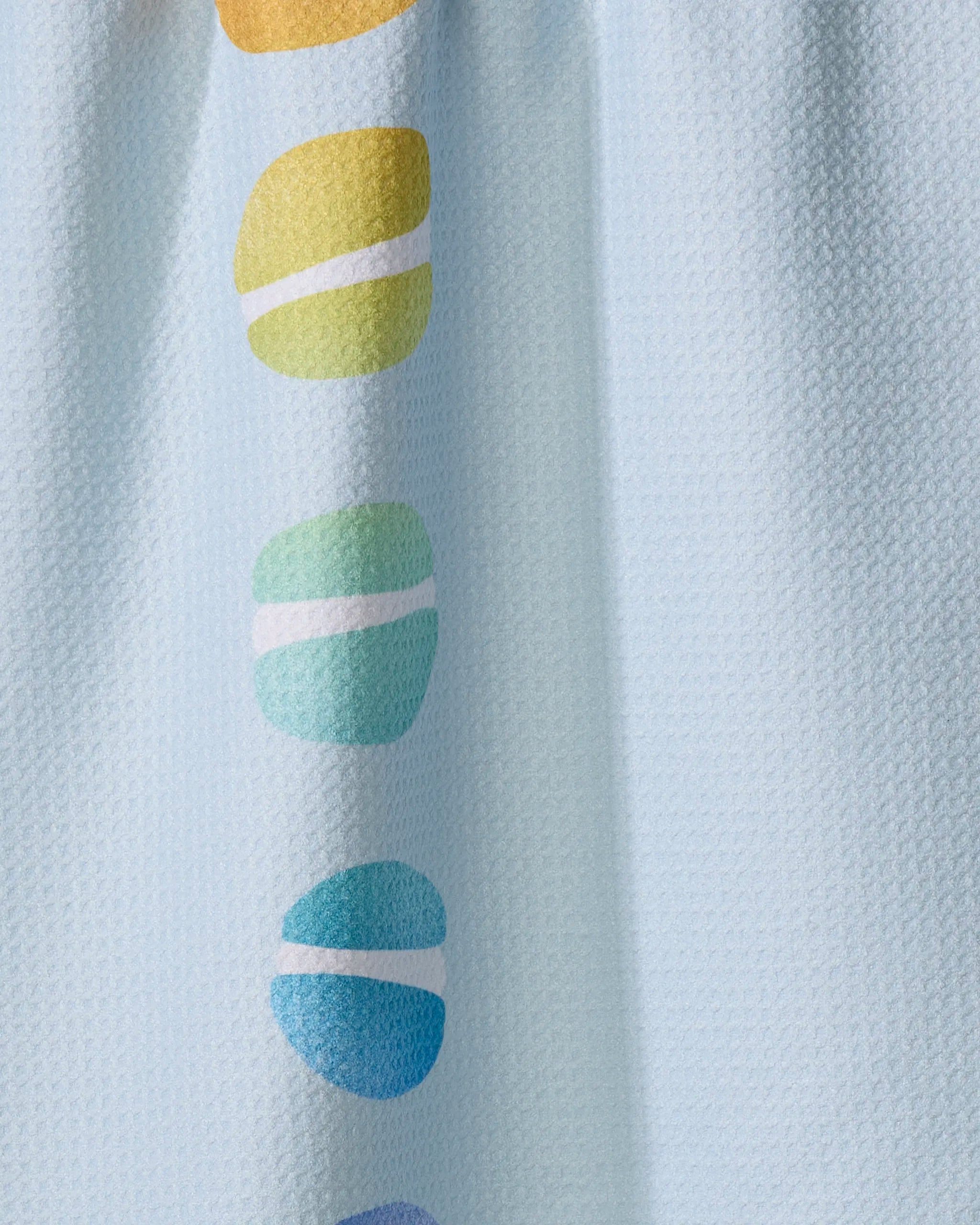 The Mac Love kitchen towel by Nora's Macarons features a textured light blue design with a vertical row of yellow, green, turquoise, blue, and purple rounded shapes—each accented by a white stripe—and is thoughtfully made from recycled materials.