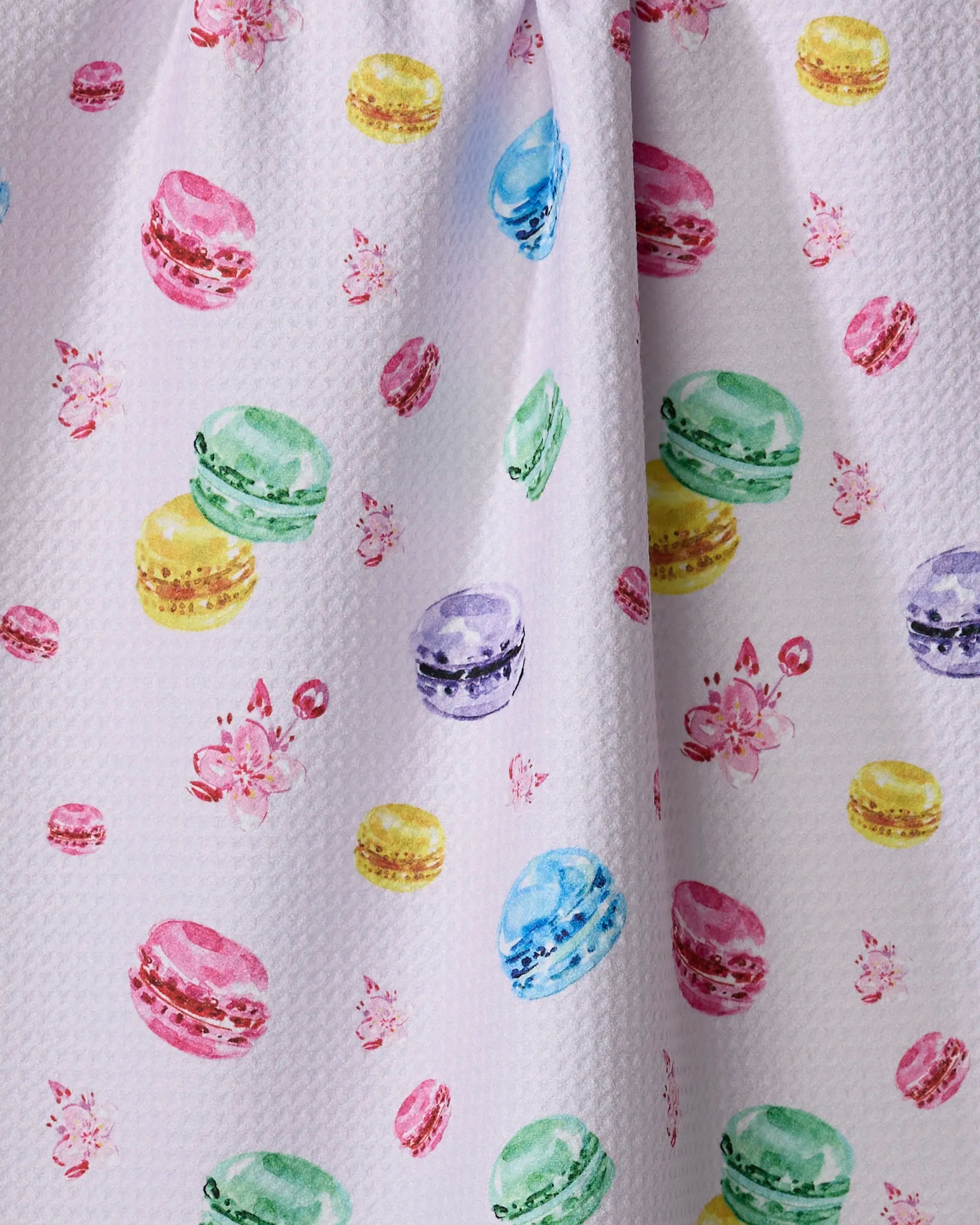 The "Macarons in Paris" tea towel by Travel Write Draw features a white textured design with colorful macarons and pink flowers, crafted from recycled materials for an eco-friendly kitchen accent.