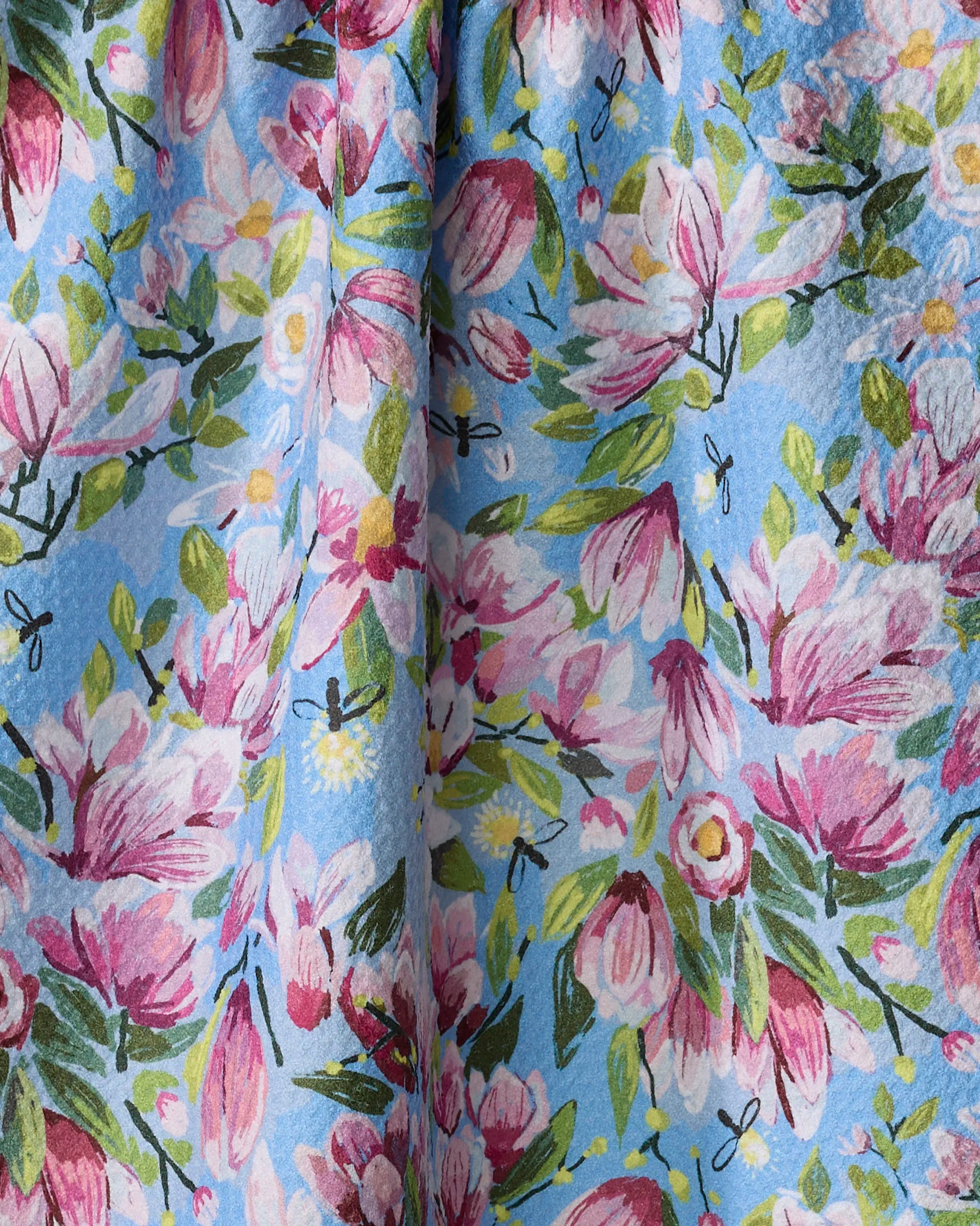 The Magnolia tea towel by Elisabeth Wing features pink and white magnolias, green leaves, and yellow accents on light blue. Made from recycled materials with a soft watercolor look, it’s stylish and absorbent—ideal for any kitchen task.