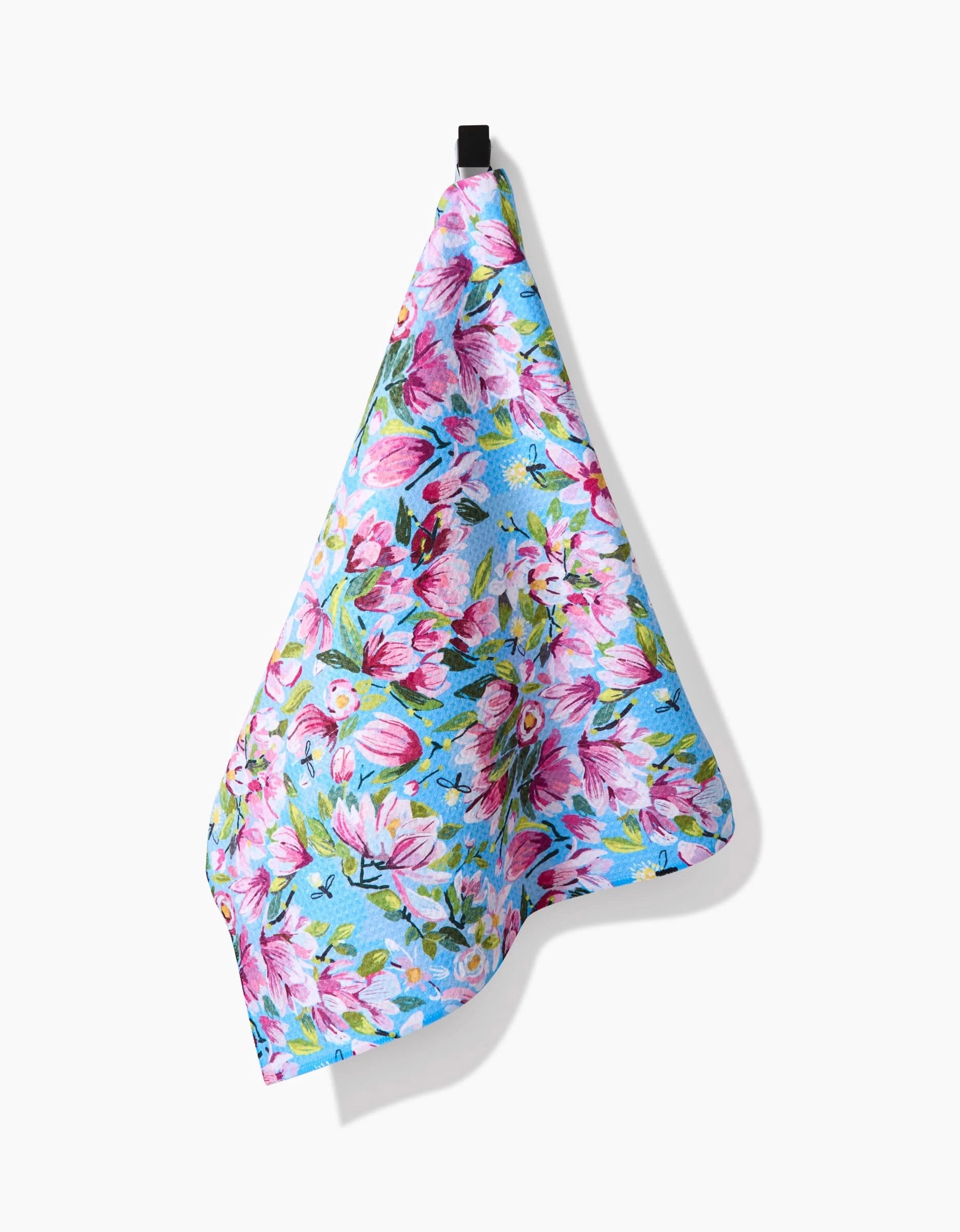 A vibrant pink and white floral Magnolia tea towel by Elisabeth Wing, made from ultra-absorbent Geoweave fabric in blue, hangs from a black loop against a plain white background.