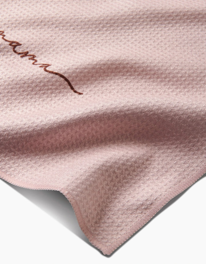 A close-up of the Kailee Wright Mama towel, in textured light pink Geoweave fabric with a subtle wavy pattern and a small Mama embroidery in brown on the upper left side.