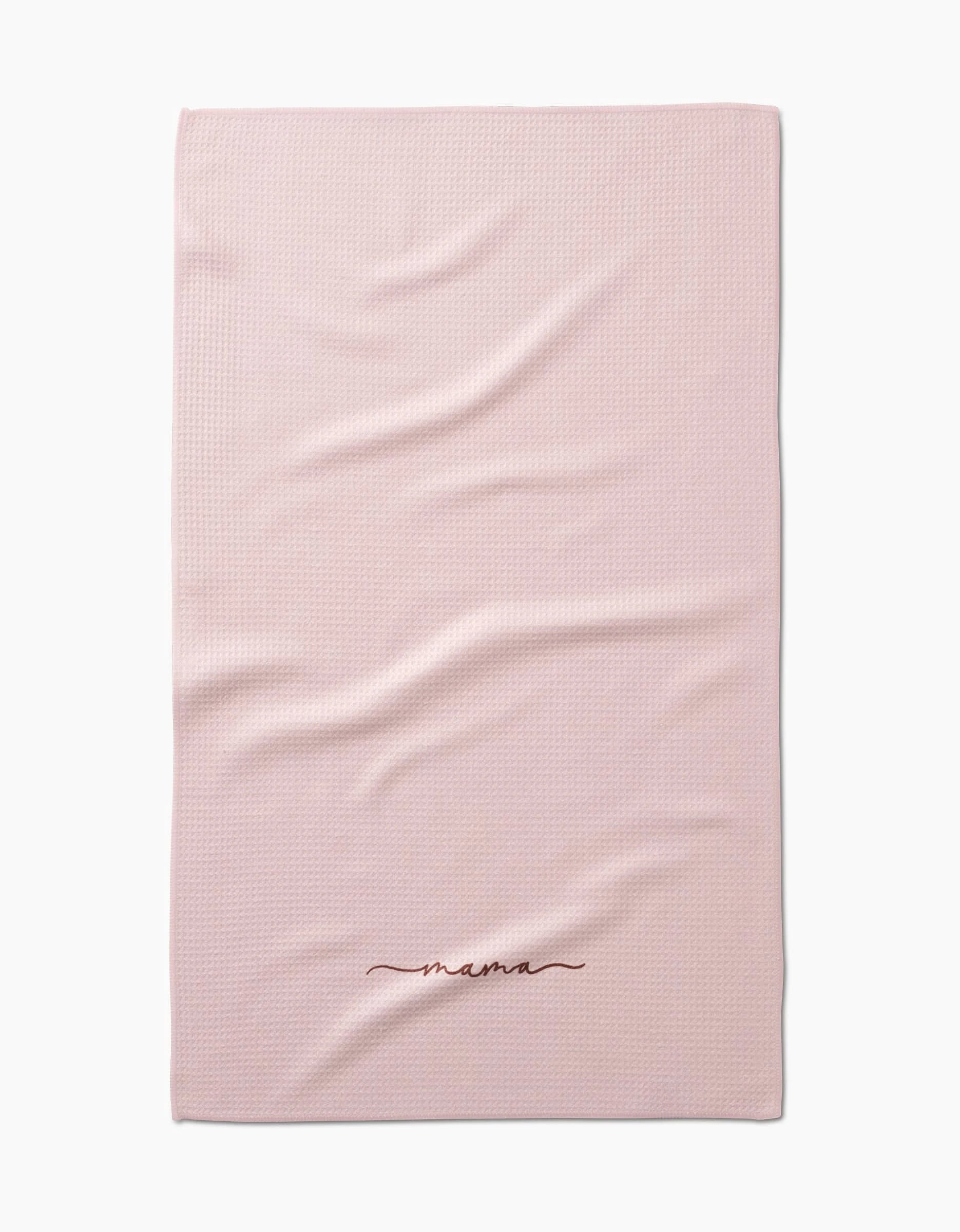 The Kailee Wright Mama blanket is light pink with a textured, ultra-absorbent Geoweave fabric and mama embroidered in dark red cursive near the edge. It’s shown laid flat with a few gentle folds.