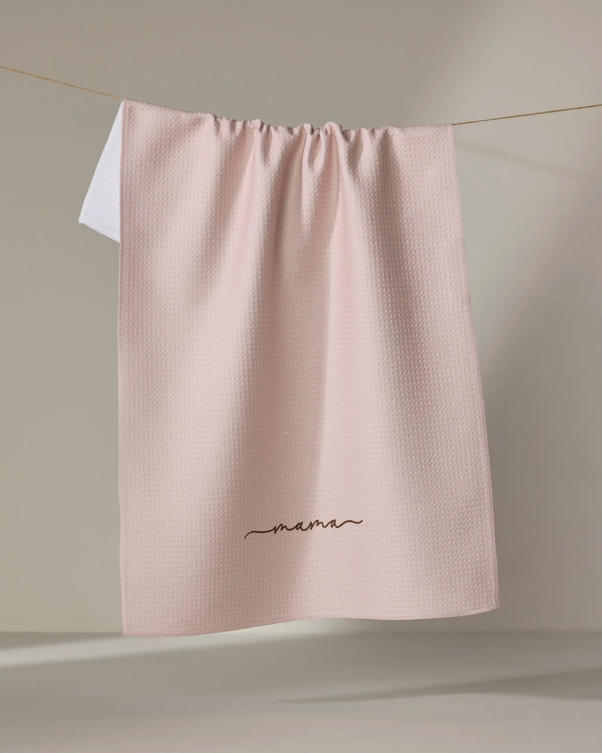 The Kailee Wright Mama blanket, in pale pink with a textured finish, is made from recycled materials and features "mama" embroidered in cursive near the bottom edge.
