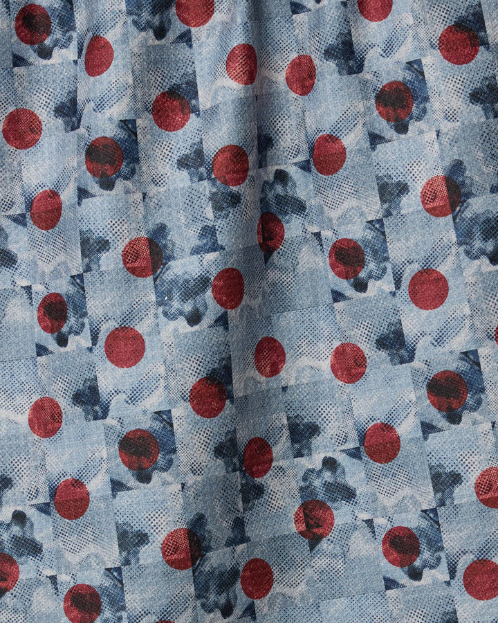 Geometry’s Manga Dot fabric features a repeating geometric pattern with large red circles and abstract blue shapes on a light blue, textured, recycled material. The surface is creased and slightly wrinkled.