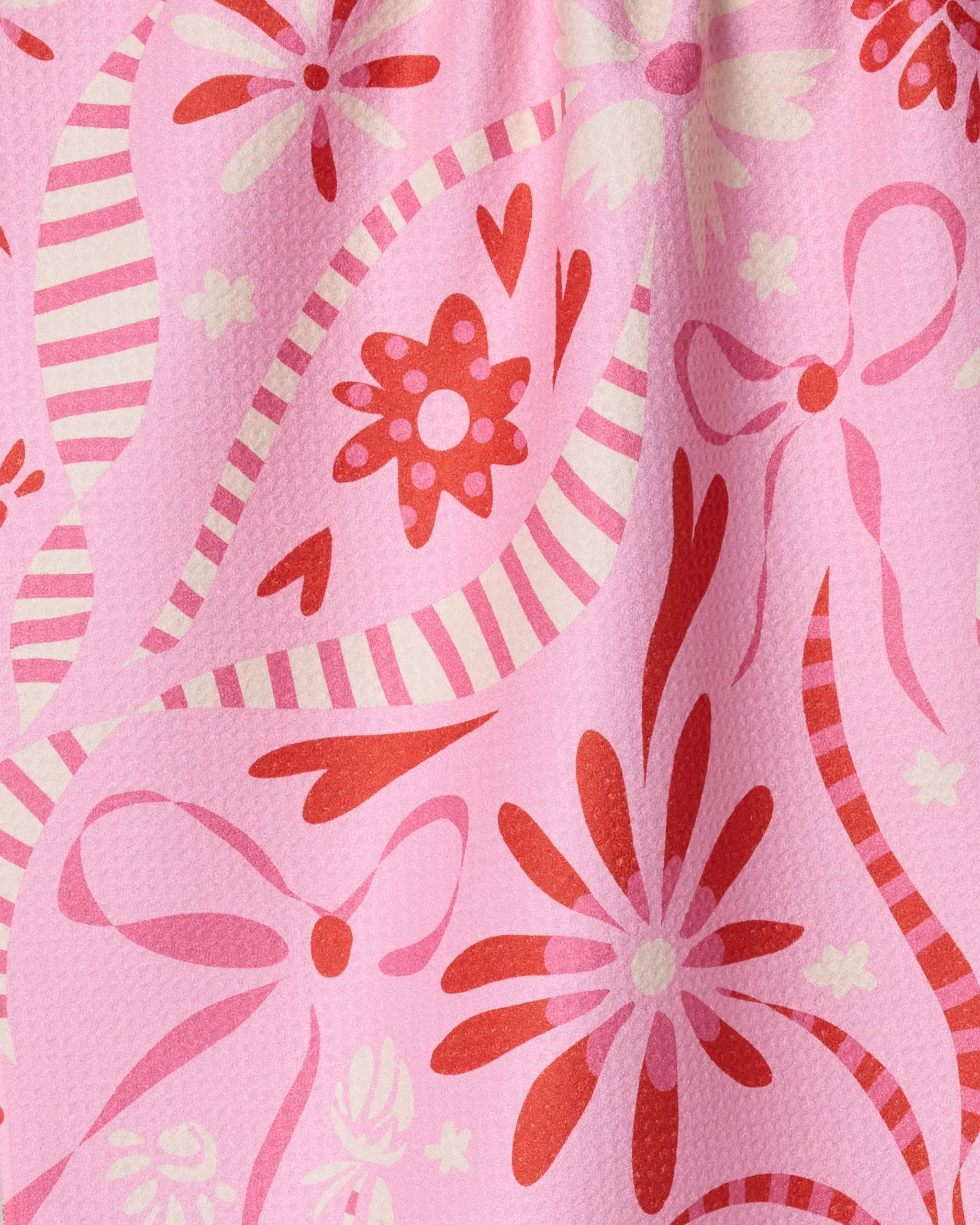 The Geometry Marcela tea towel features a whimsical floral and ribbon pattern in red, pink, and white on a light pink background. Crafted from absorbent materials, it brightens any kitchen with its playful design.