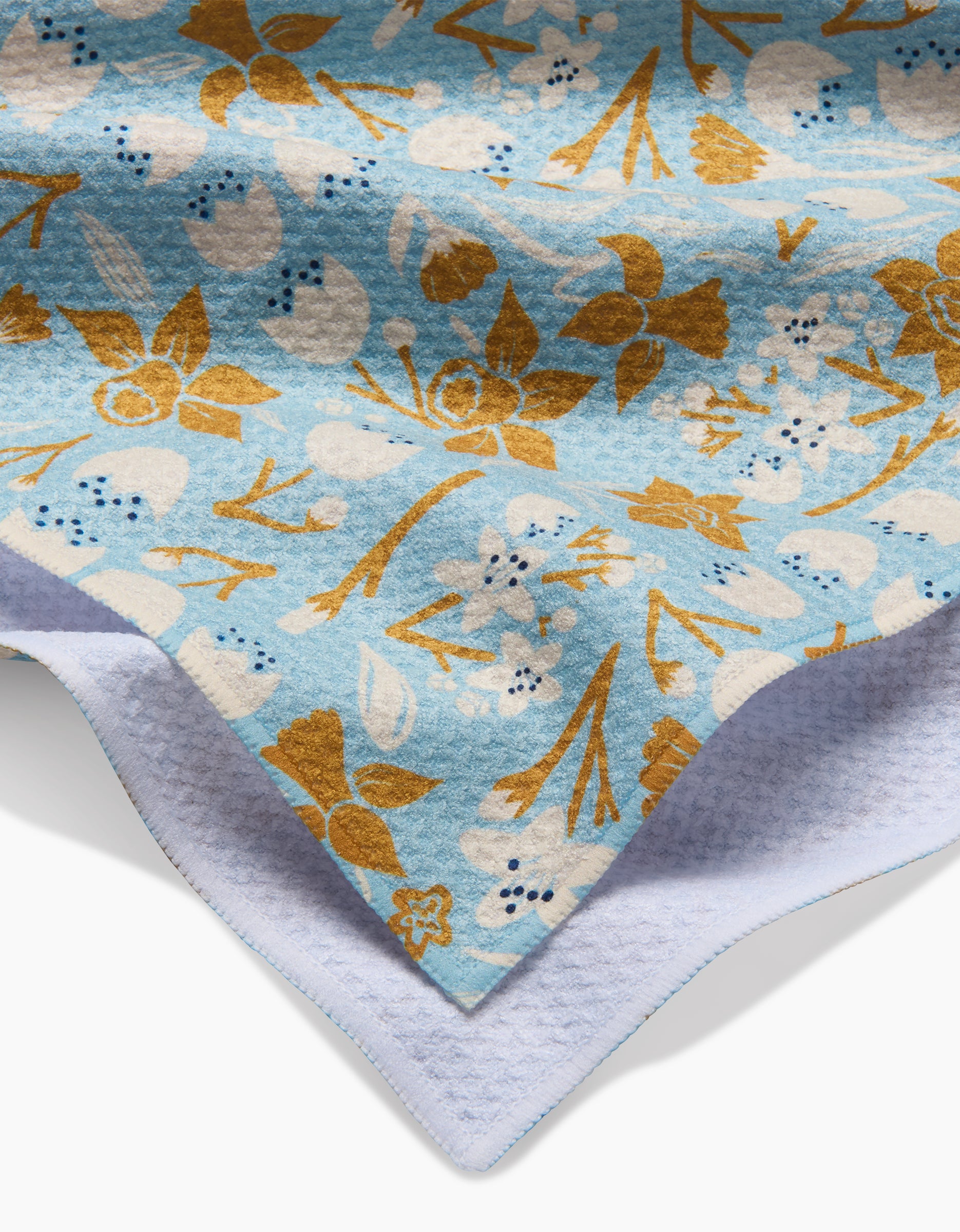 A close-up of the March blanket by Elisabeth Wing, featuring a light blue surface with yellow and white floral patterns on top and a white Geoweave™ fabric underside, displayed against a white background.