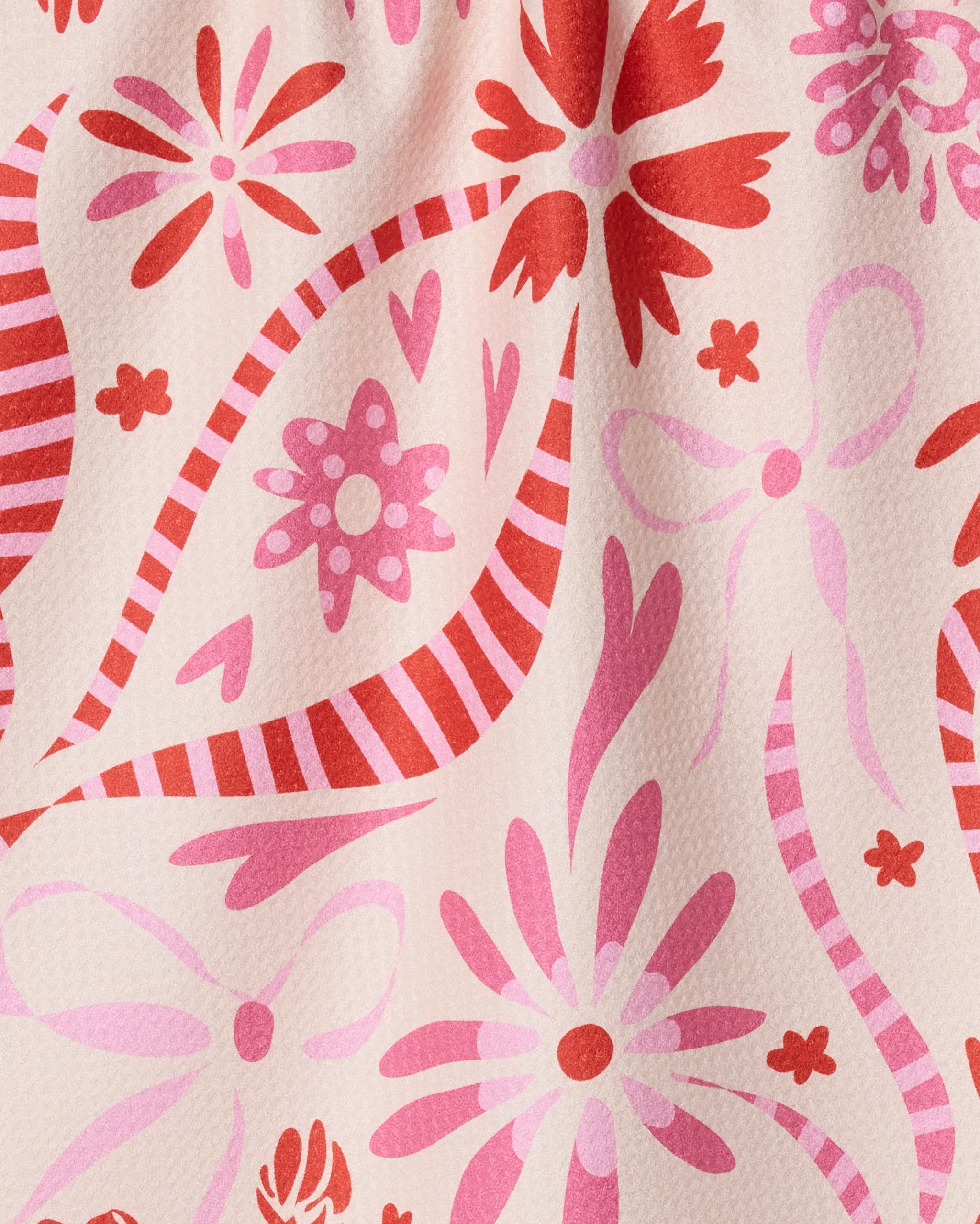 A close-up of the Maricela tea towel by Geometry, made from recycled materials, features a pink and red floral pattern with flowers, leaves, and wavy stripes on a pale background. The fabric has a slightly wrinkled appearance.