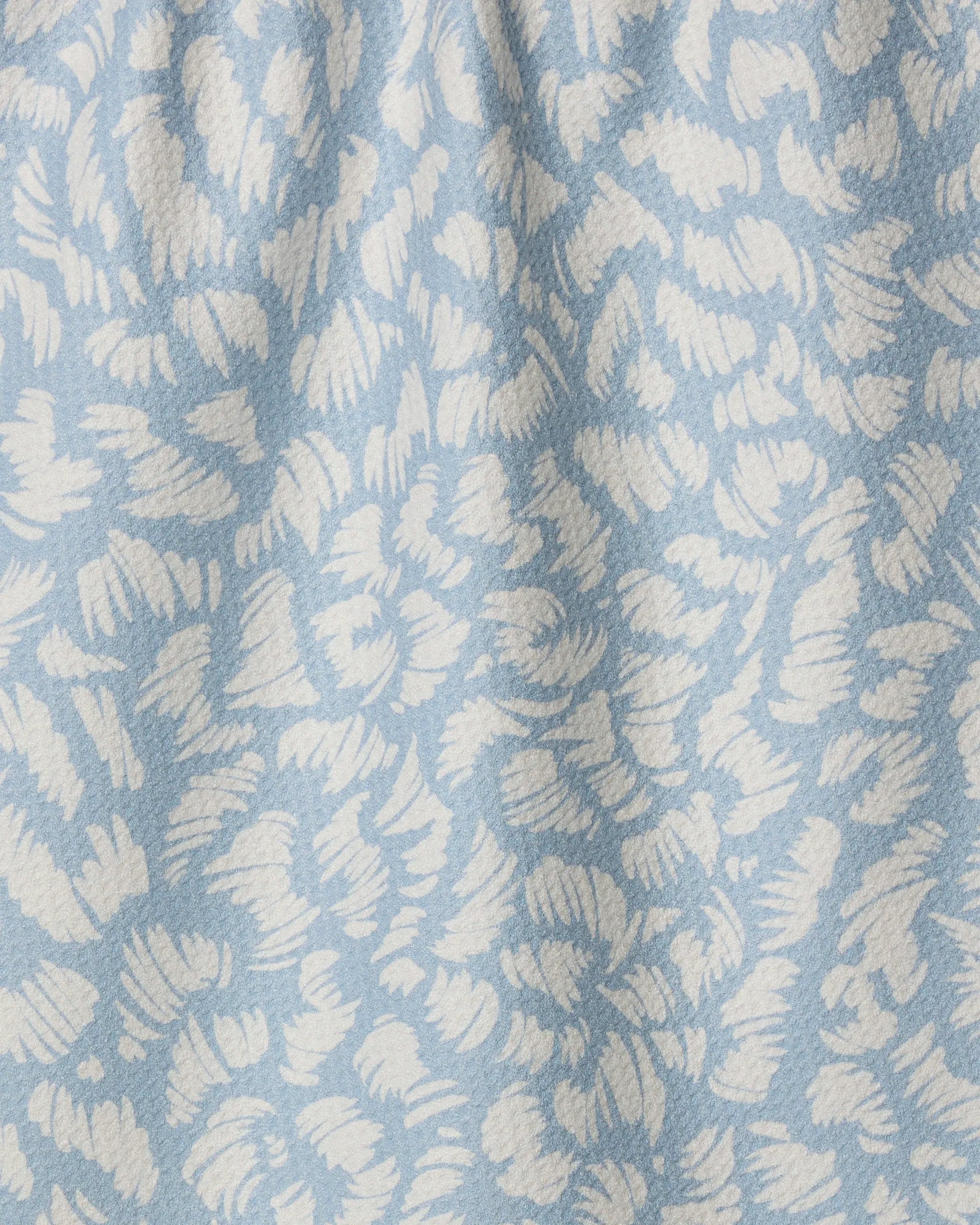 Close-up of Marine Haze by Geometry, a light blue tea towel made from recycled materials with a white abstract floral or leaf design, featuring a subtly textured surface and gentle folds.