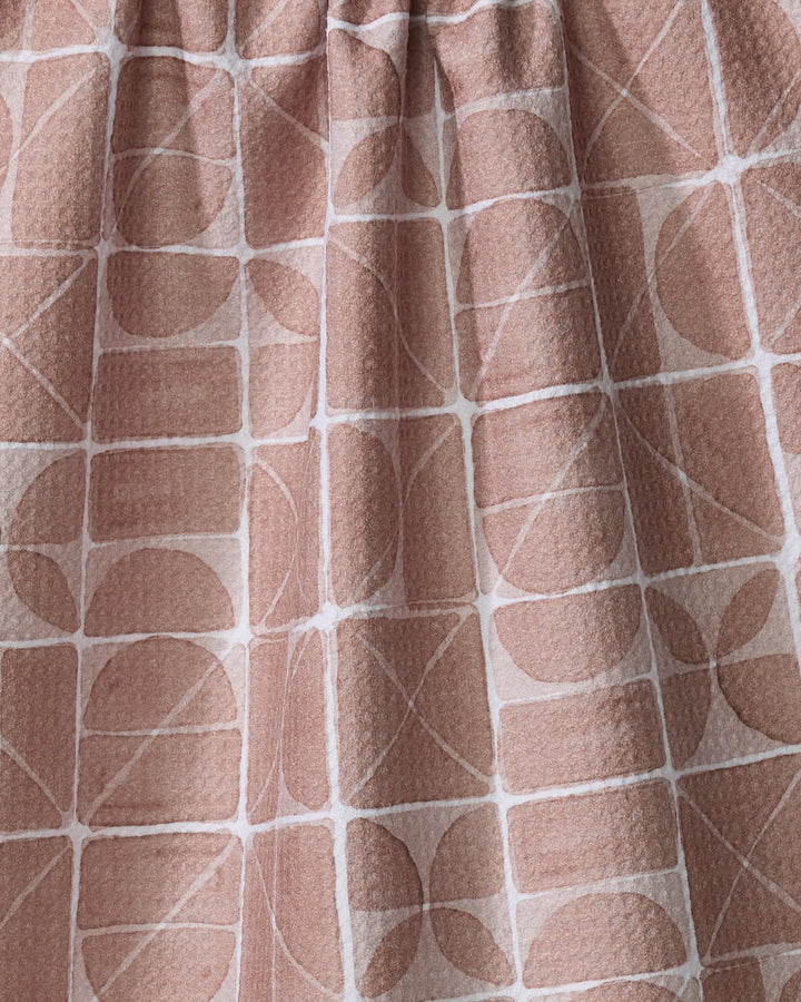 A close-up of Mariposa by Studio Jeannot, a tea towel featuring pinkish-beige fabric with a textured surface and a grid-like geometric pattern of white lines, circles, semi-circles, and rectangles—an elegant kitchen essential.