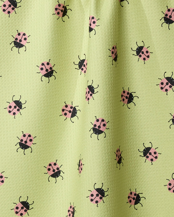 The Geometry Mariquita kitchen towel features a light green recycled fabric with a textured feel and a repeating pattern of pink and black ladybugs scattered across the surface.